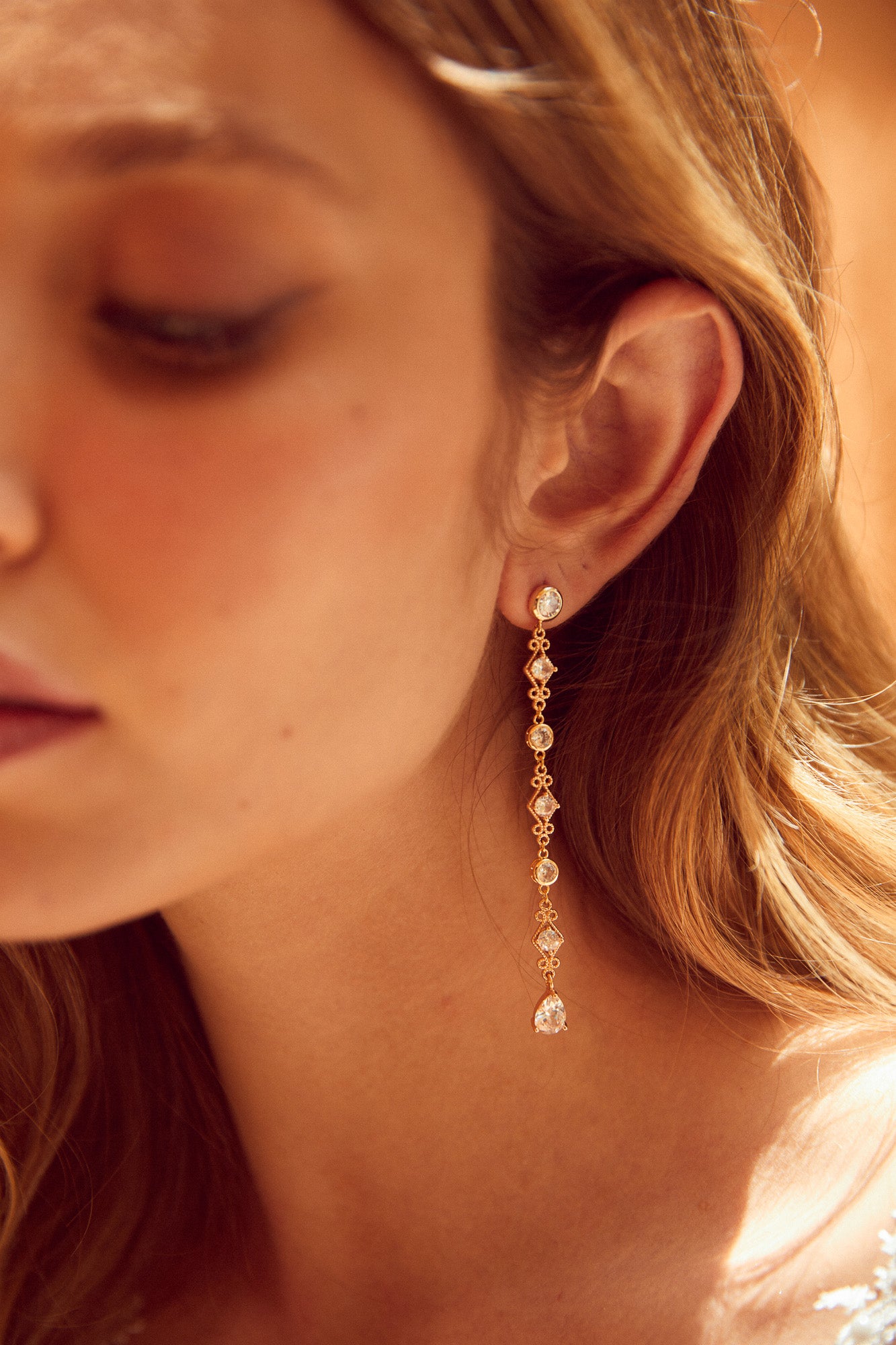 mariée portant des boucles d'oreilles longues pendantes en or et cristaux style vintage et romantique prise de près par le photographe