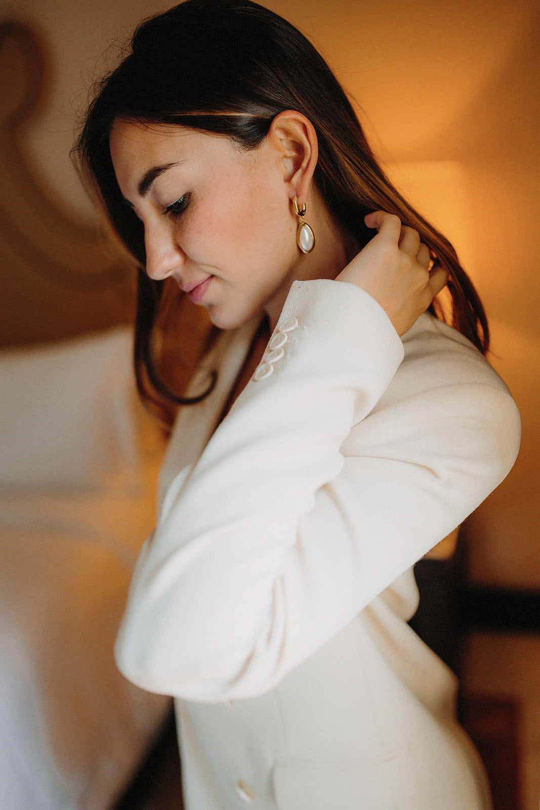 boucles d'oreilles minimaliste porté par une mariée en blazer avec les cheveux détachés qui touche ses cheveux pour montrer la boucles d'oreilles