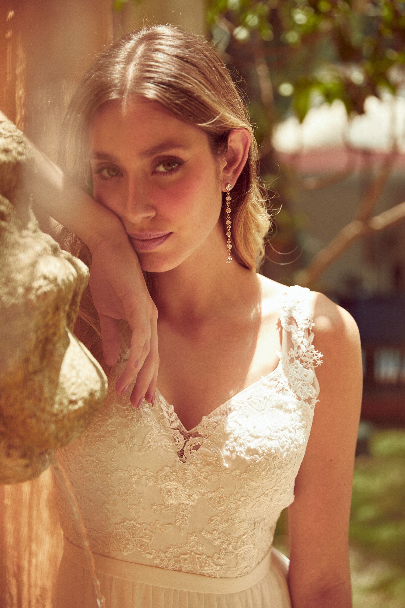 mariée portant des boucles d'oreilles longues pendantes en or et cristaux style vintage et romantique souriante