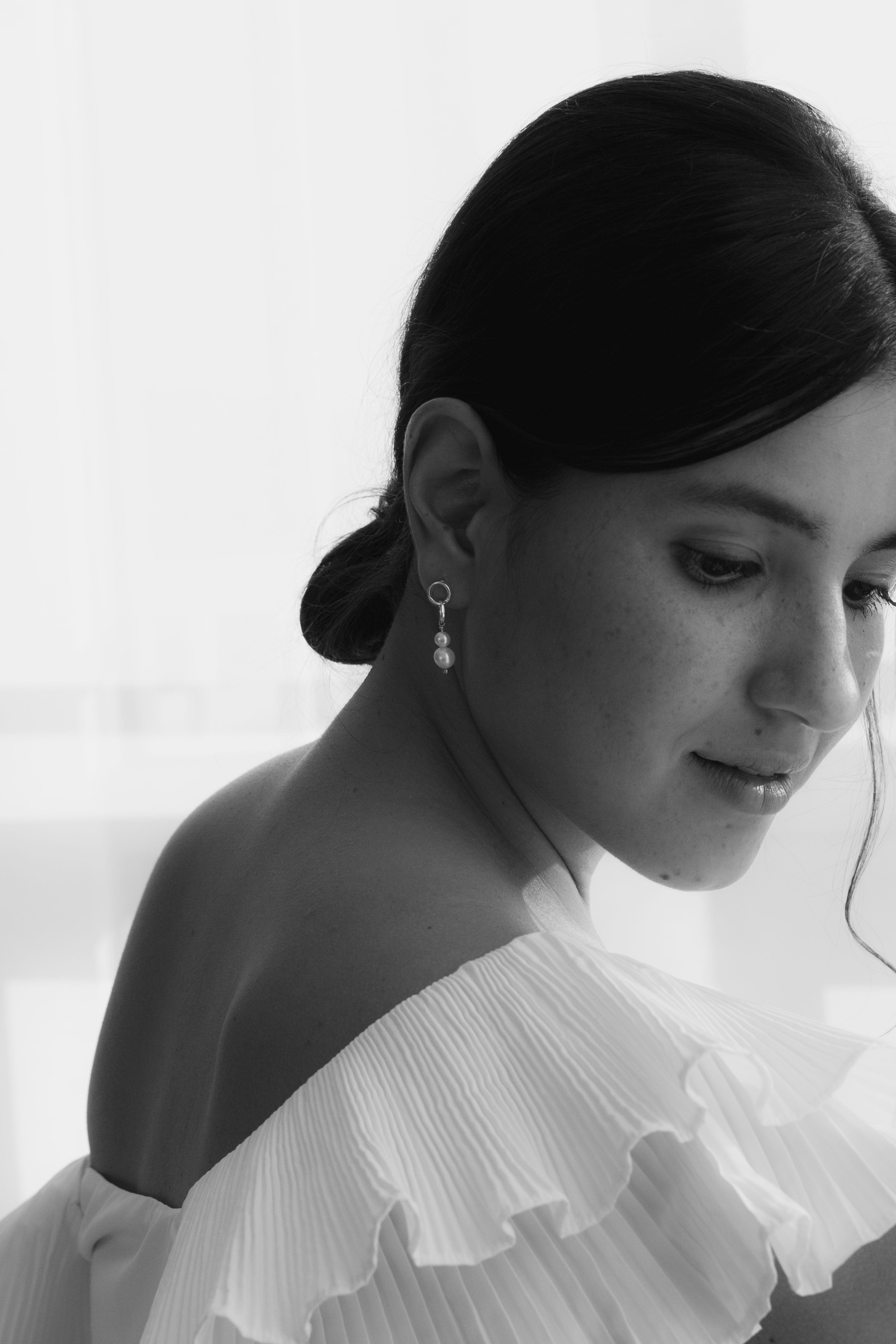 Mariée en noir et blanc avec chignon sophistiqué bas et boucles d'oreilles pendantes à doubles anneaux dorés et deux perles naturelles blanches