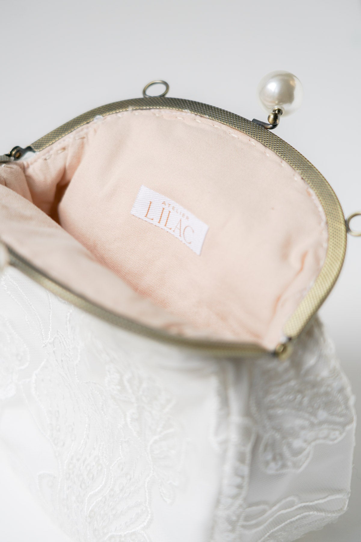 sac de mariage blanc ouvert cousu avec un tissu en dentelle fleuri et une attache bronze avec deux perles