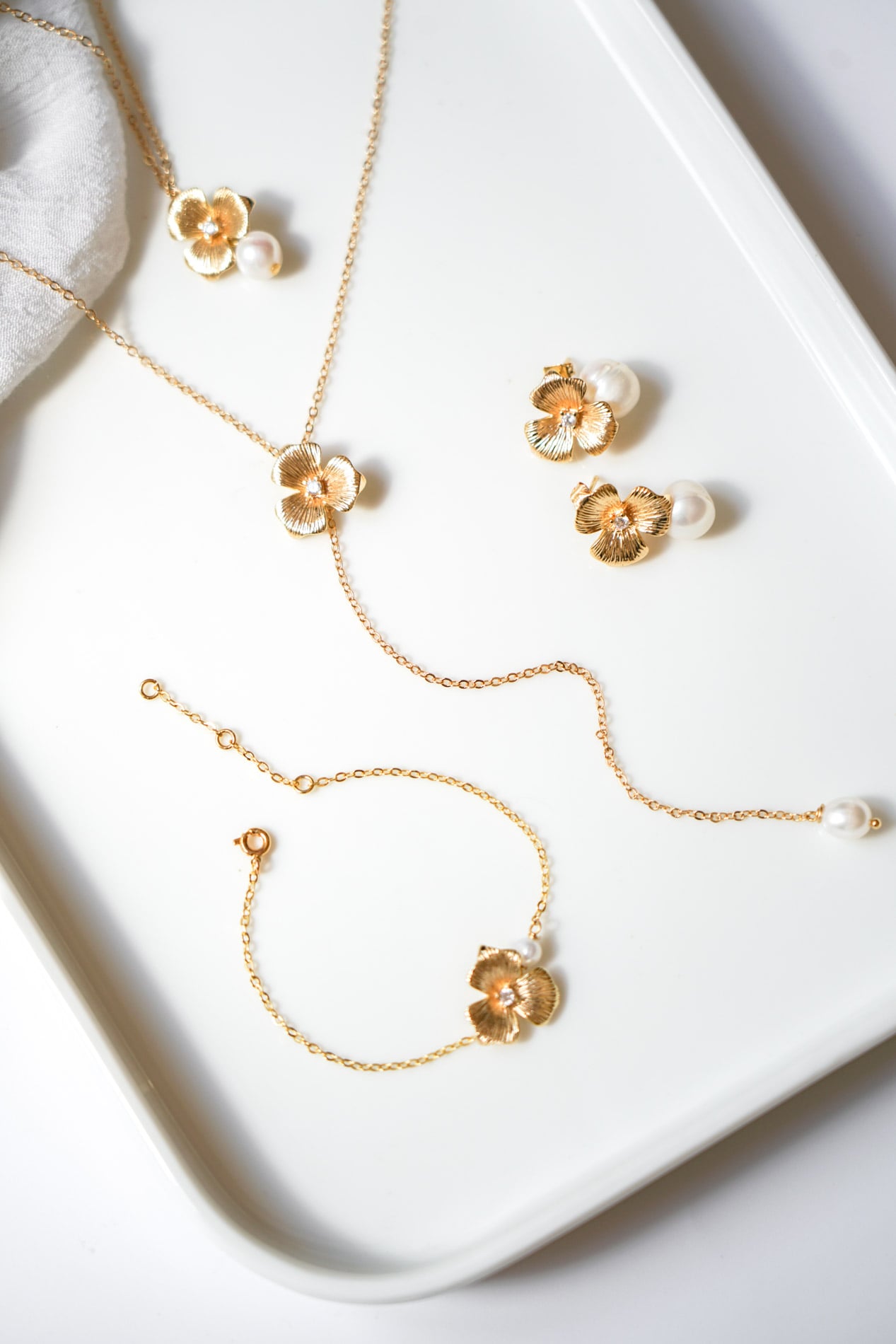 parure de bijoux mariage avec des fleurs et des perles naturelles sur un plateau blanc