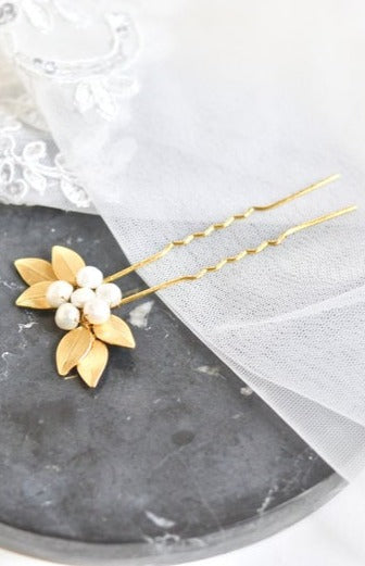 pic de cheveux mariage en forme de fleurs formé avec des feuilles en or et un coeur en perles posé sur un plaque de marbre noir