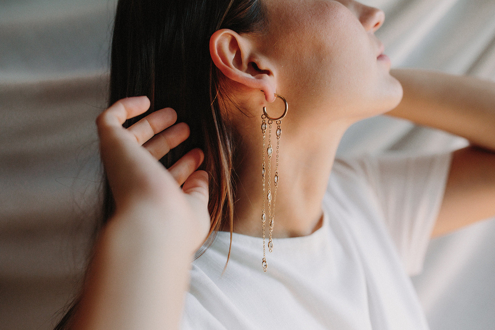 Mariée portant des boucles d'oreilles pendantes élégantes avec un anneau doré duquel pendent trois chaines en or ornées de cristaux