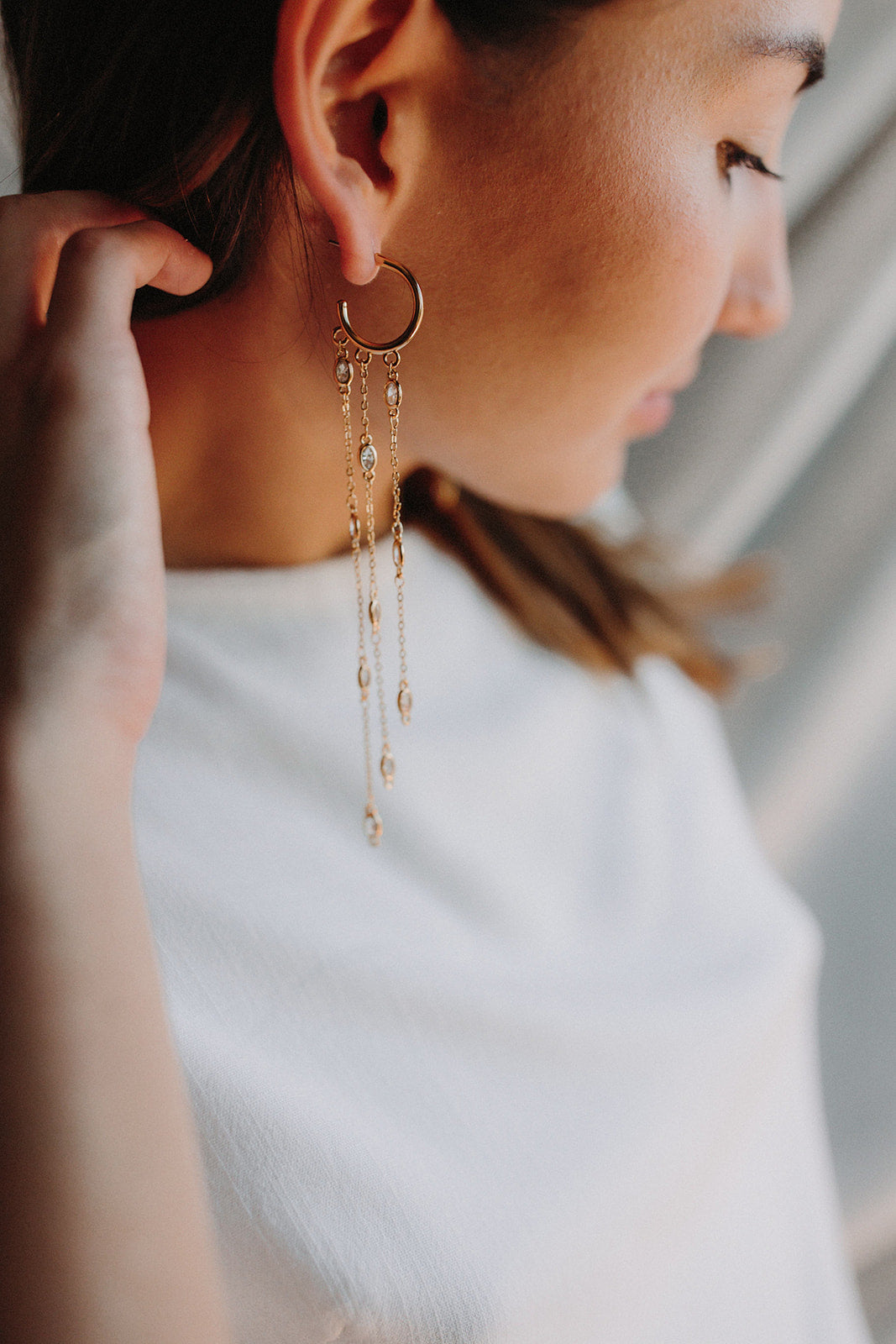 Mariée portant des boucles d'oreilles pendantes romantiques avec un anneau en or duquel pendent trois chaines ornées de cristaux