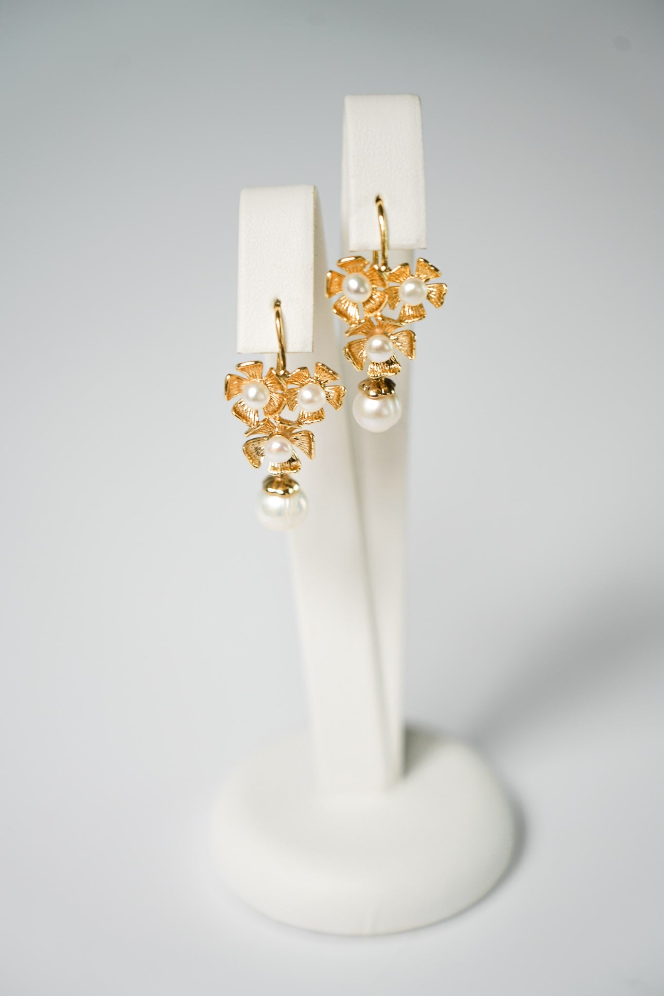 Boucles d'oreilles trois fleurs dorées ornées de perles sur un support