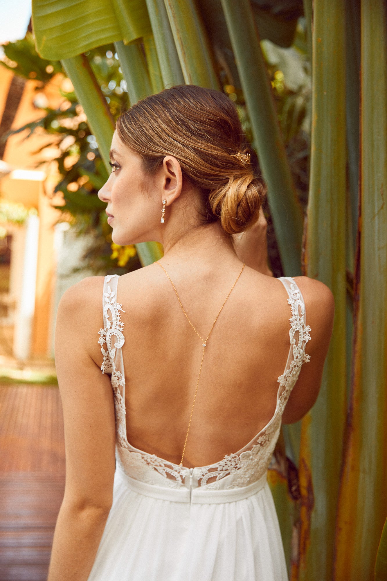 mariée de dos portant un collier de dos et des boucles d'oreilles assorti ainsi qu'un peigne sur un chignon bas