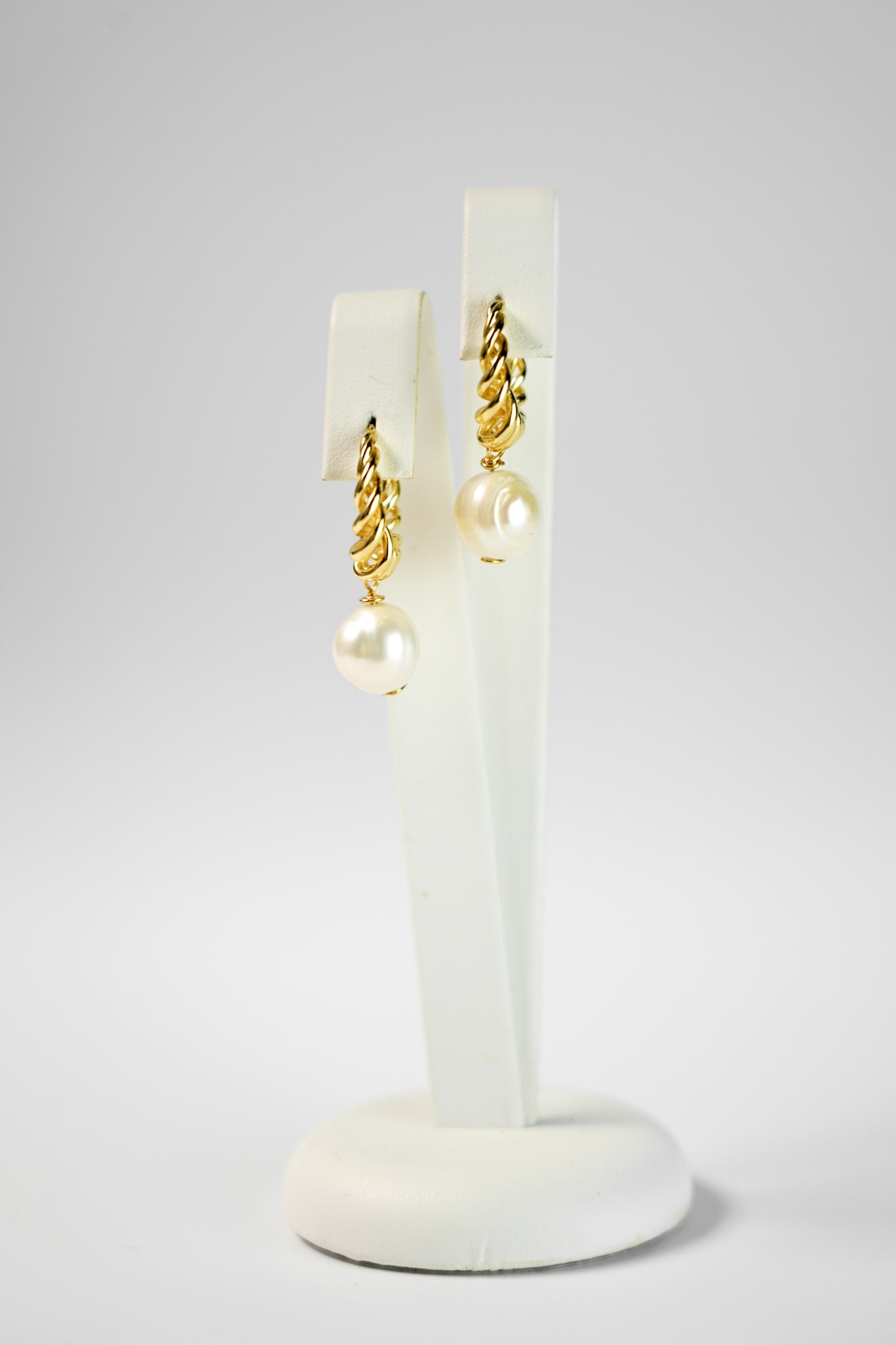 Boucles d'oreilles créoles entrelacées dorée avec une perle sur un socle blanc