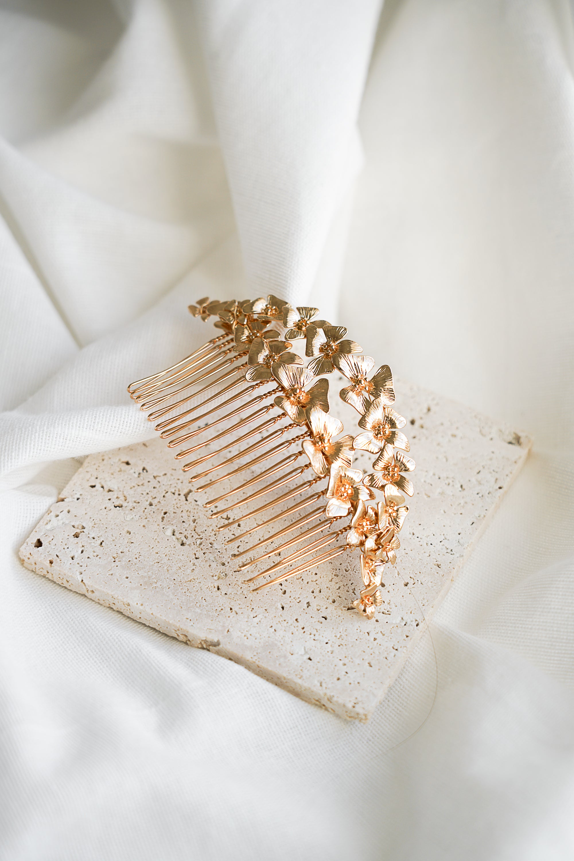 peigne de mariage floral bohème sur deux rangs de fleurs en or posé sur un fond blanc