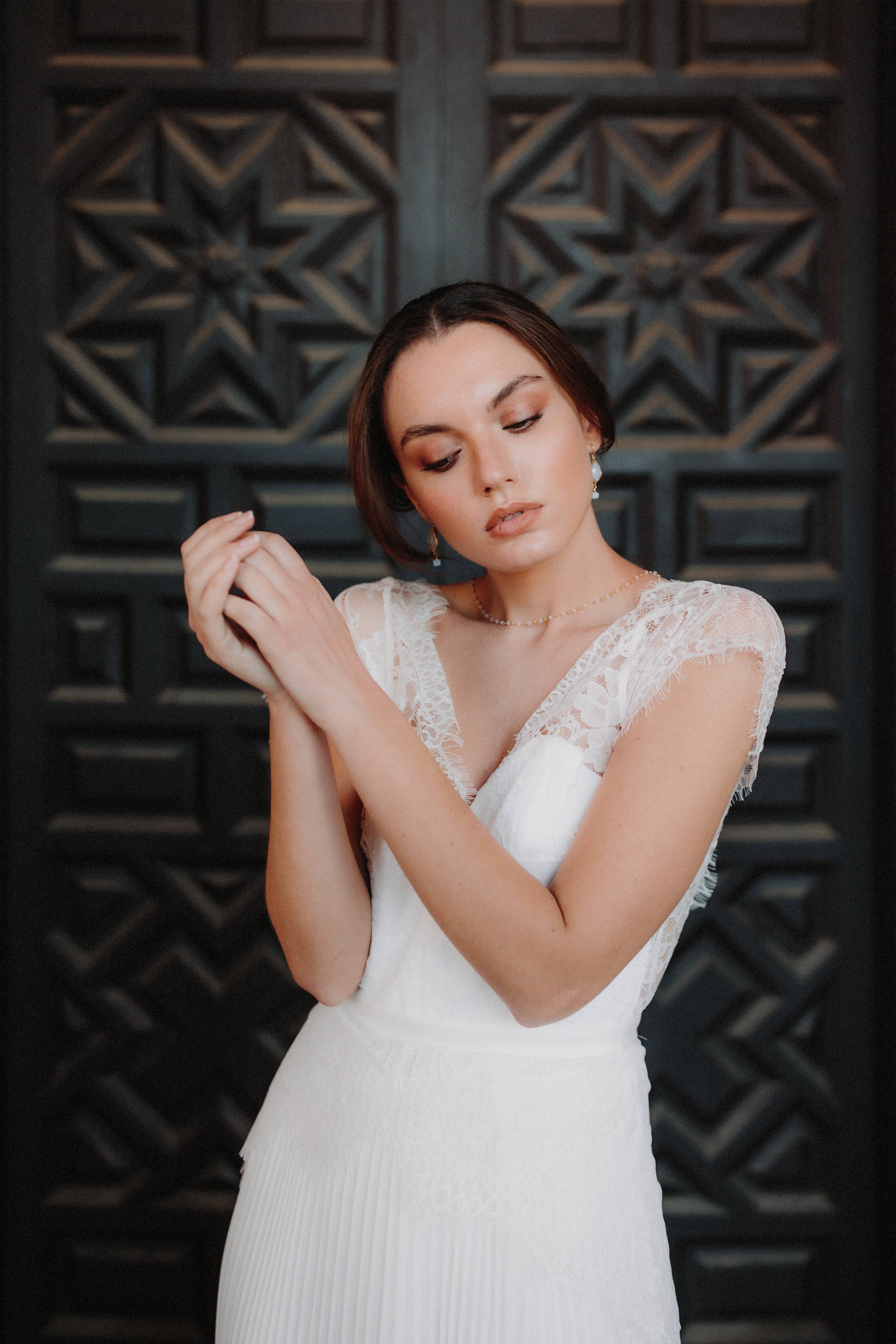 mariée en robe blanche à dentelle portant des boucles d'oreilles en pierres naturelles pendantes