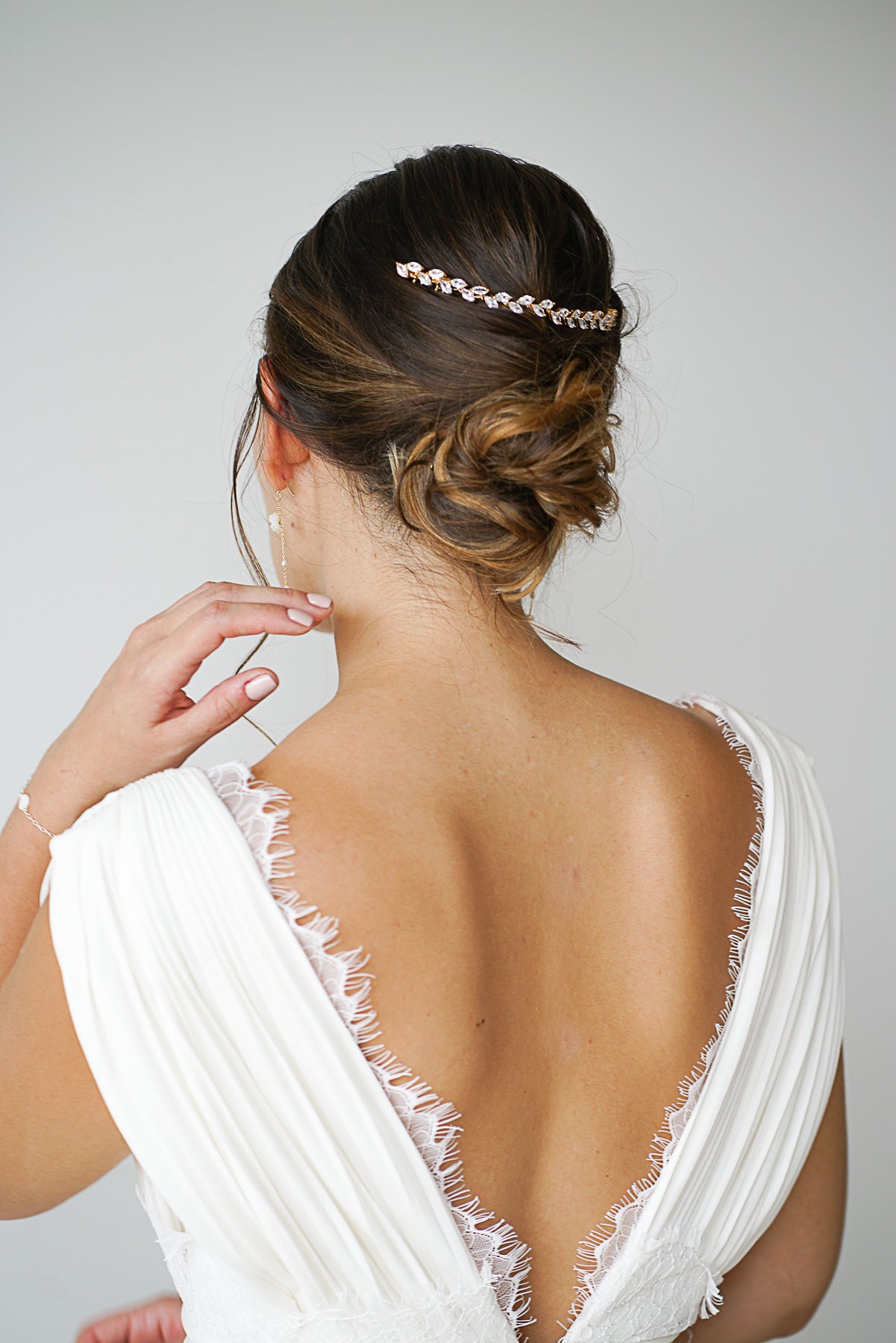 Mariée avec un chignon de mariage coiffé décoiffé et une vigne à cheveux romantique faite de feuilles en cristaux