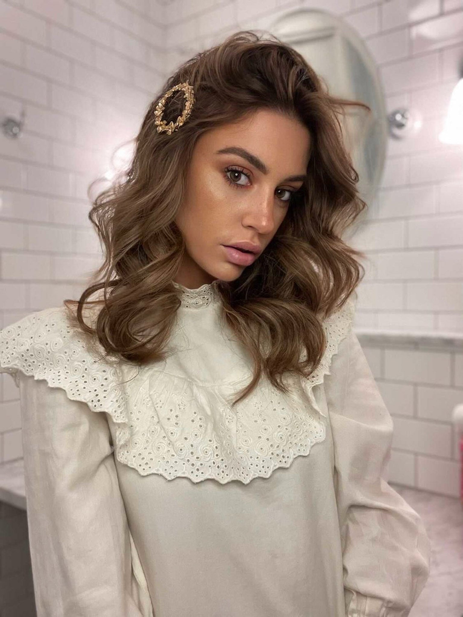 Femme portant une barrette à cheveux à fleurs dorées dans une salle de bain blanche