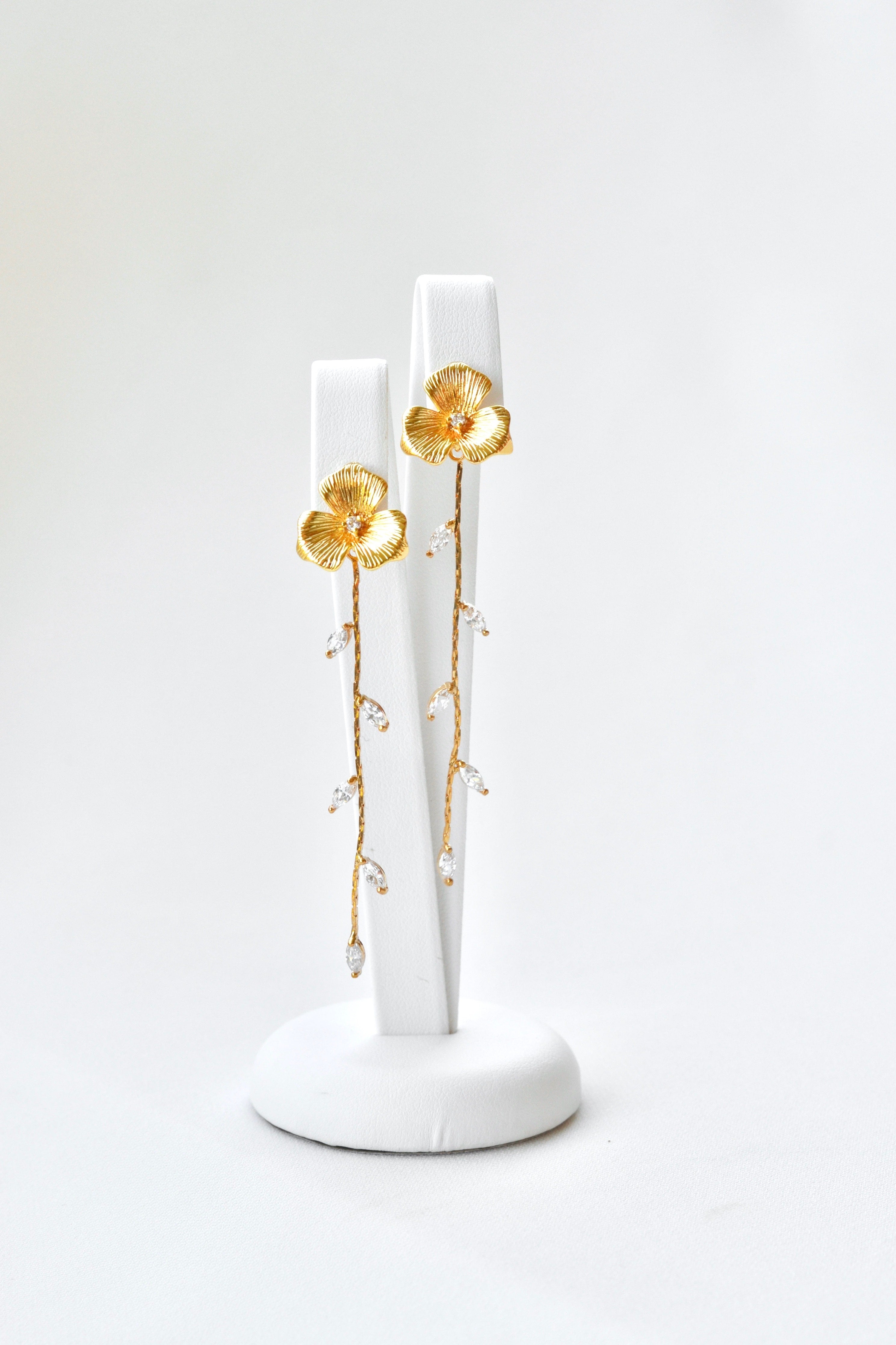 Boucles d'oreilles pendantes fait à la main avec une fleur pour le centre de la boucle et une blanche de feuilles en pendentif sur un fond blanc