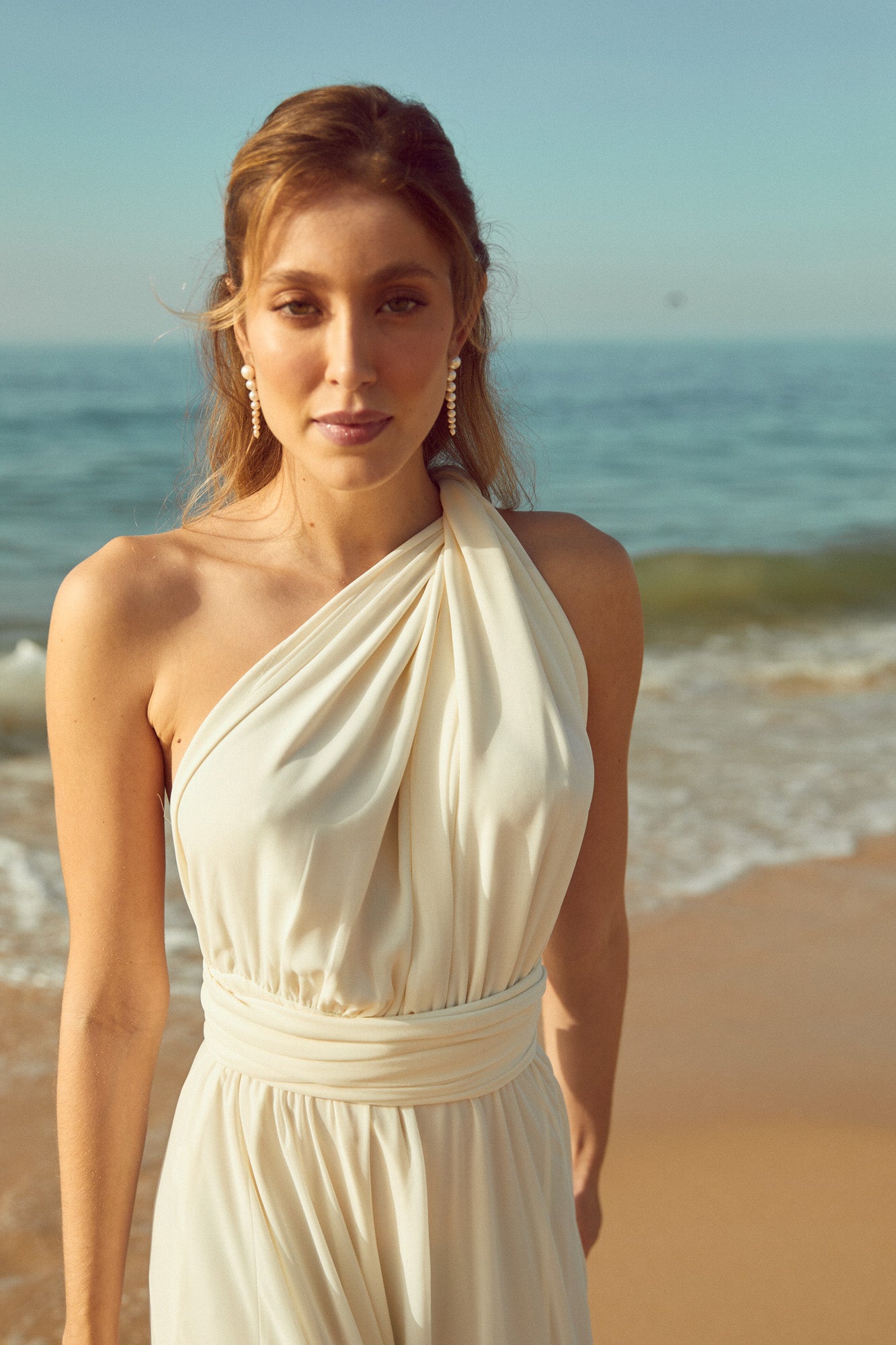 mariée sur la plage qui porte des boucles d'oreilles en perles et une robe blanche