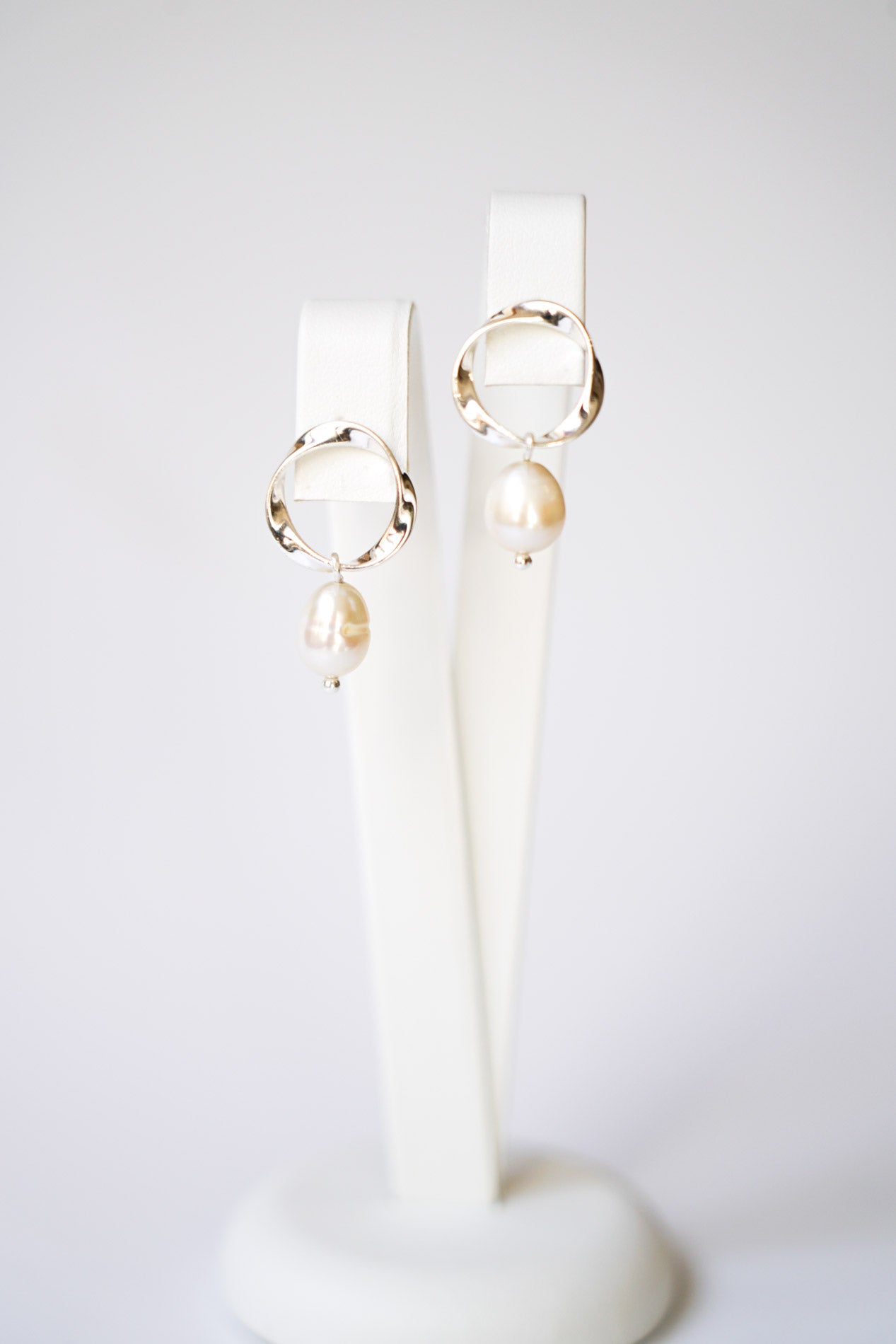 boucles d'oreilles ronde en forme de spirale avec comme pendentif une perle naturelle bohème et moderne sur un socle à bijoux