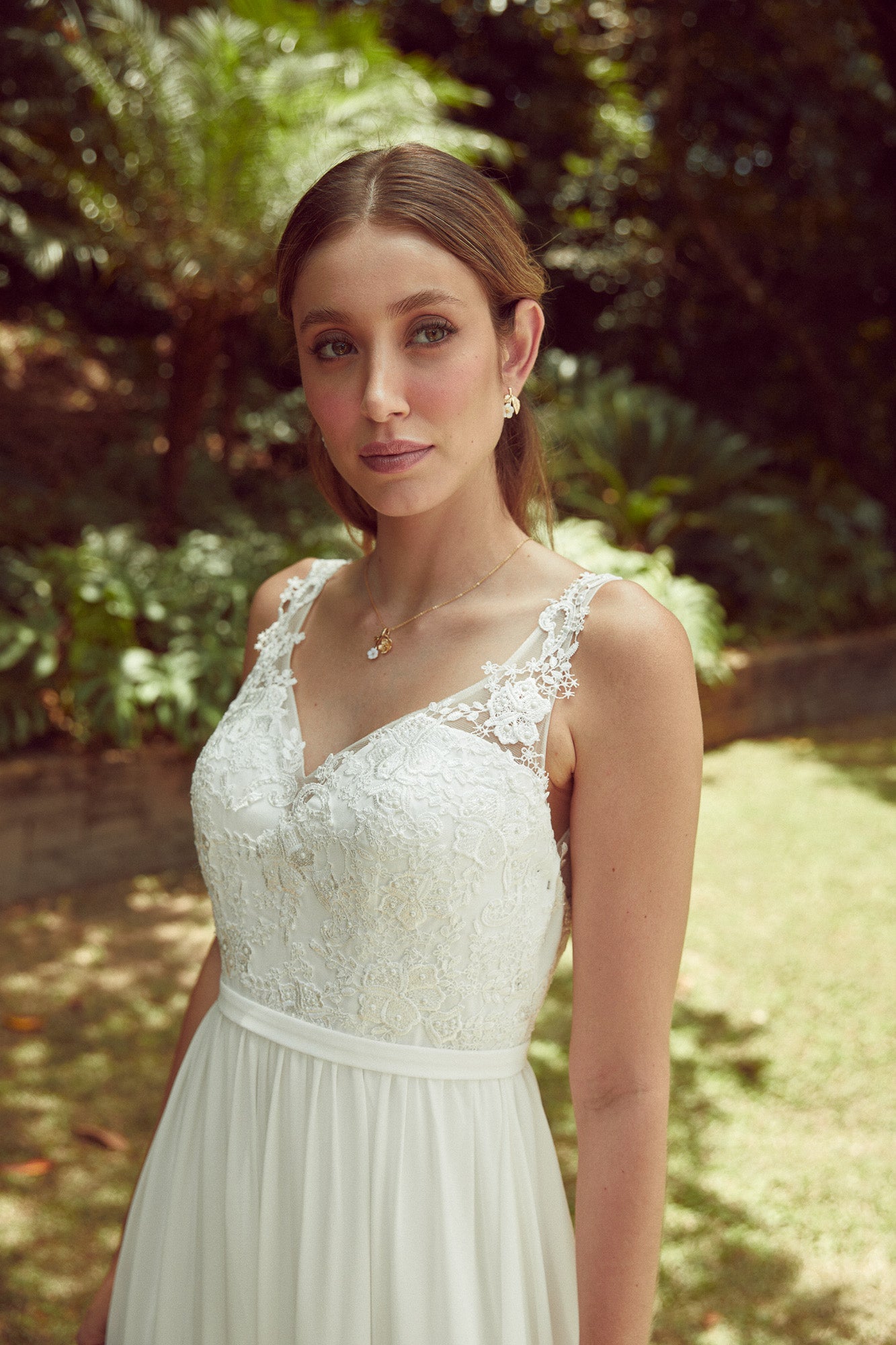 Mariée au style romantique avec un collier or à fleurs or et blanches et boucles d'oreilles fleuries blanche et or