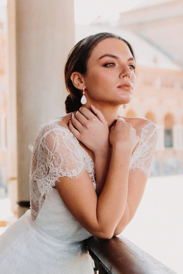 mariée portant une robe de mariage blanche avec de la dentelle et des boucles d'oreilles en forme d'ovale blanc