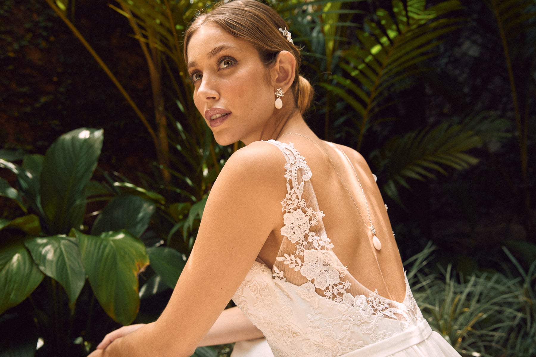 mariée dans la nature portant un collier de dos assorti a ses boucles d'oreilles en nacre regardant vers le haut