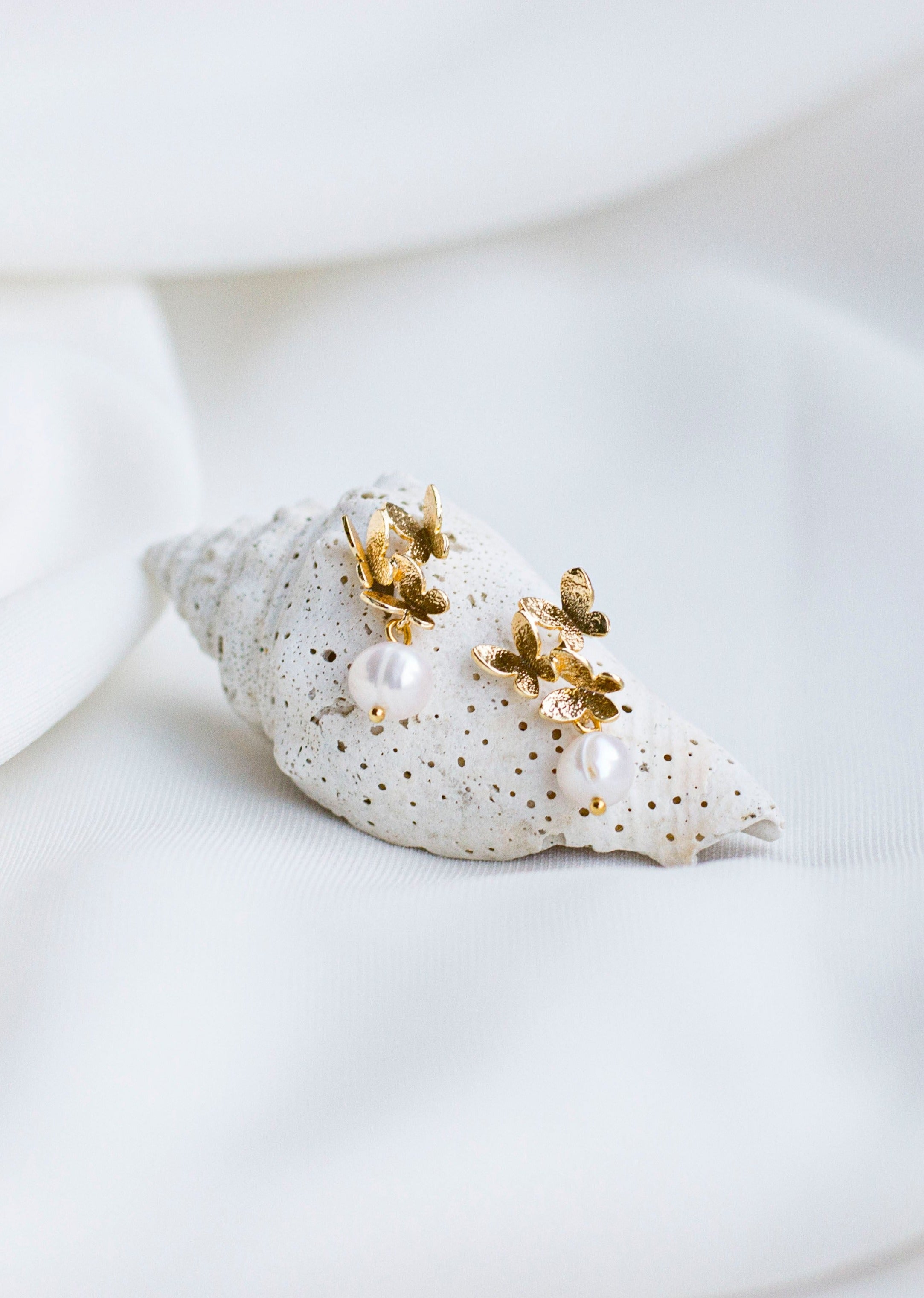 Boucles d'oreilles mariage papillons dorées et perles naturelles sur un coquillage