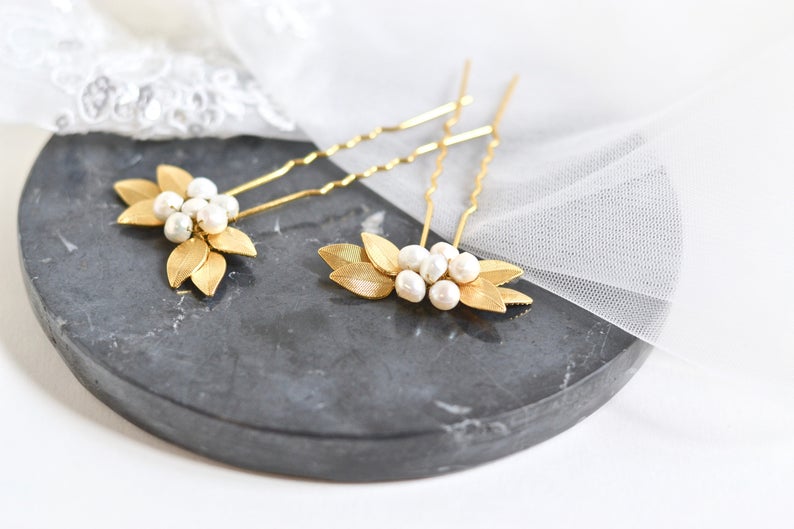 pic de cheveux mariage avec des feuilles en or et un coeur en perles posé sur un bout de marbre