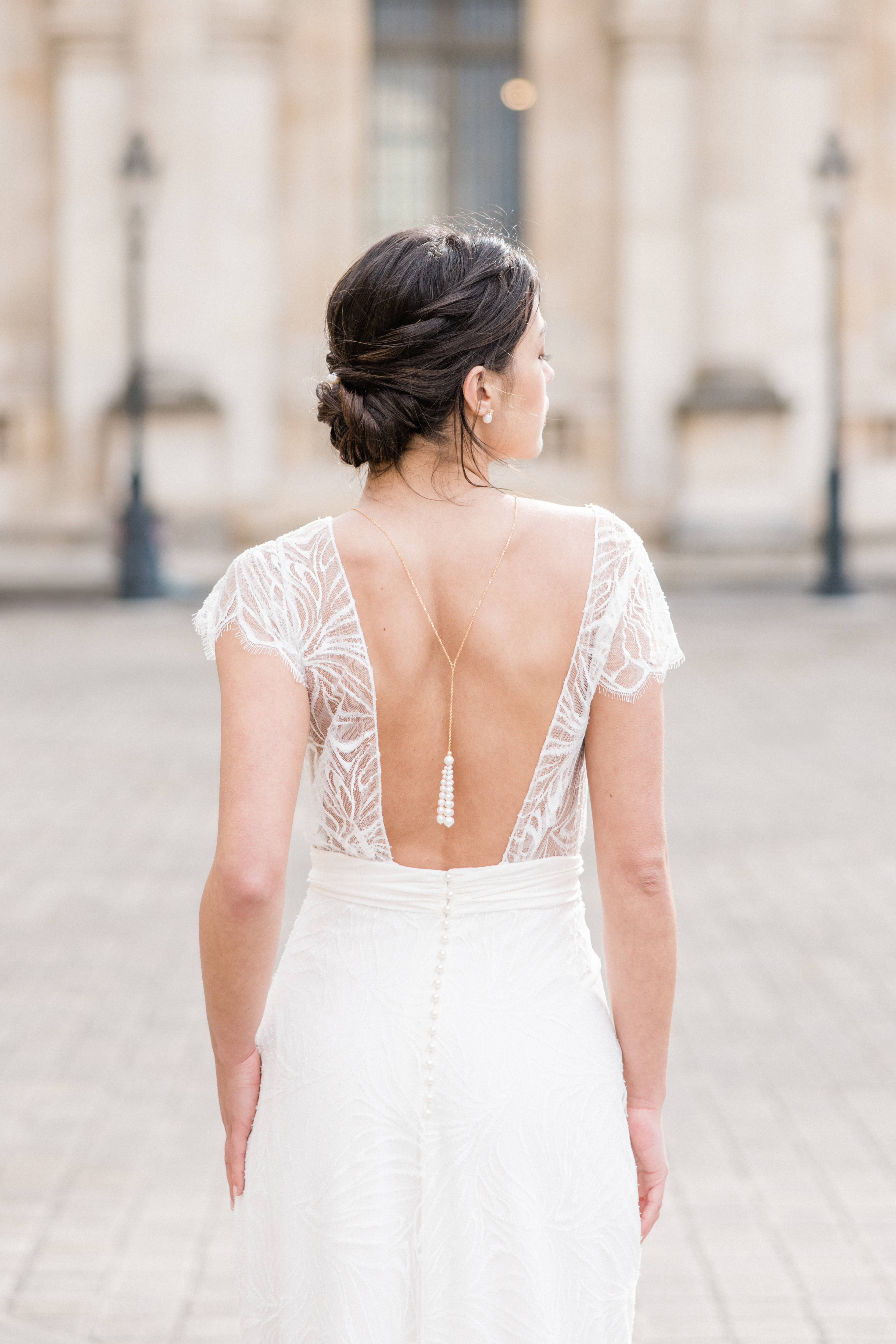 Mariée avec grand décolleté de dos dans une robe en dentelle accessoirisé d'un collier de dos à pompom de perles