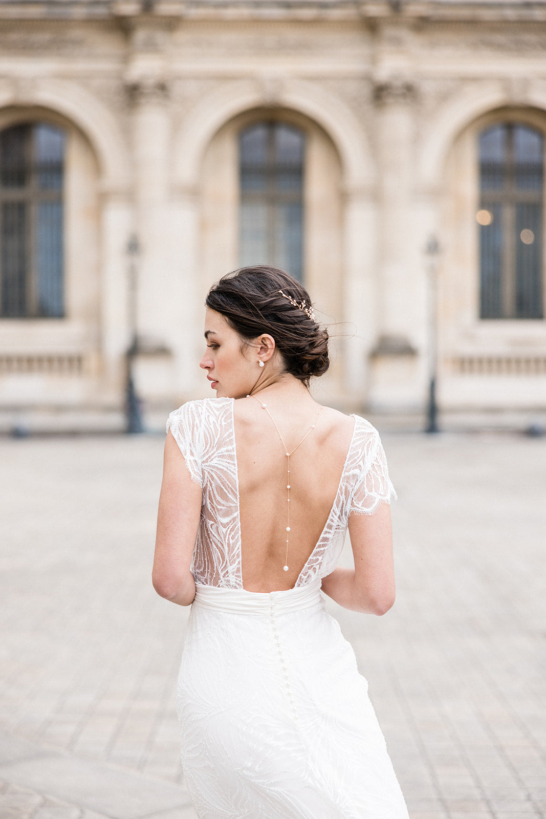 Mariée portant un collier de dos et des boucles d'oreilles romantiques à perles et une vigne à cheveux romantique dorée