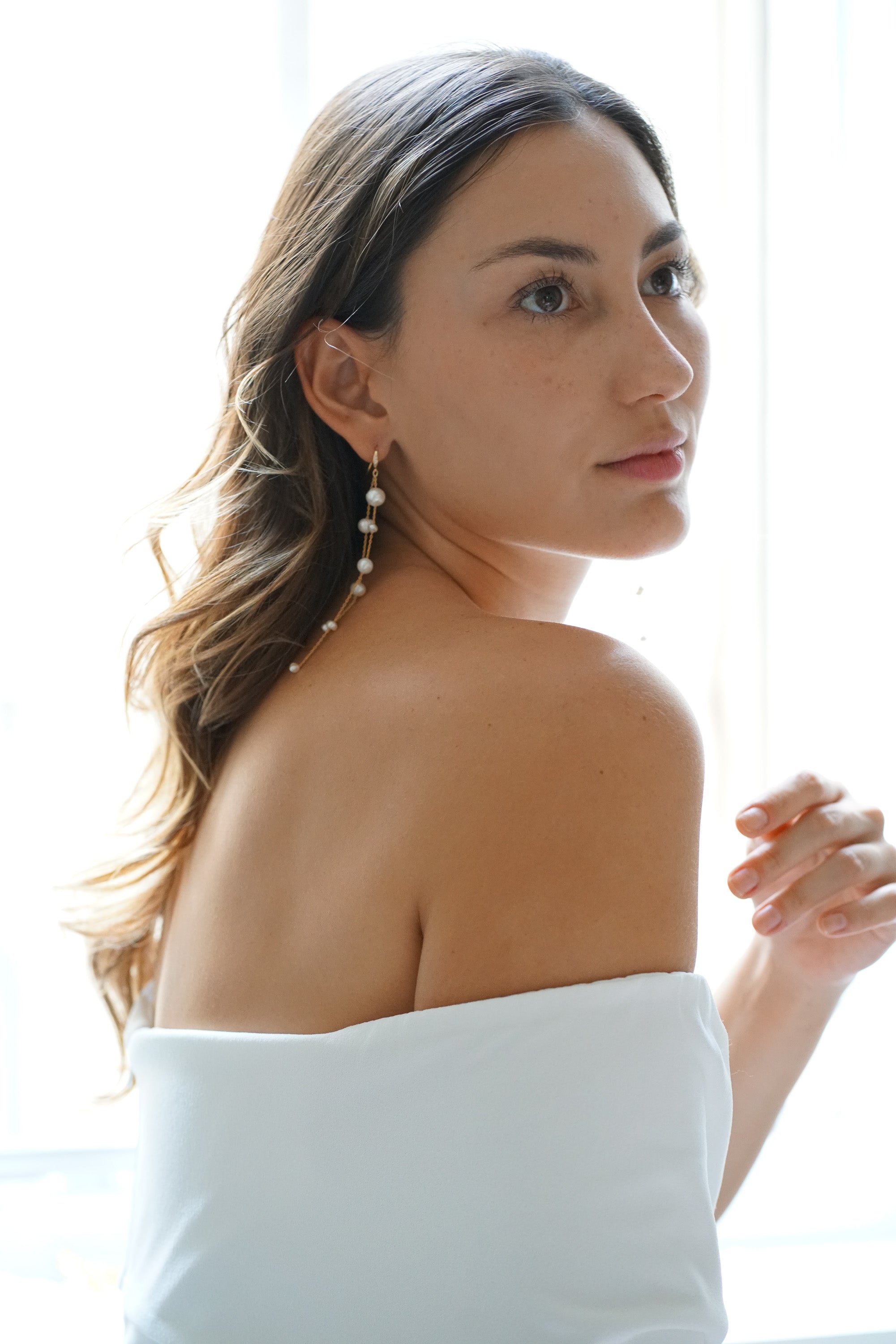 Mariée portant des boucles d'oreilles pendantes à perle et robe épaules dénudées