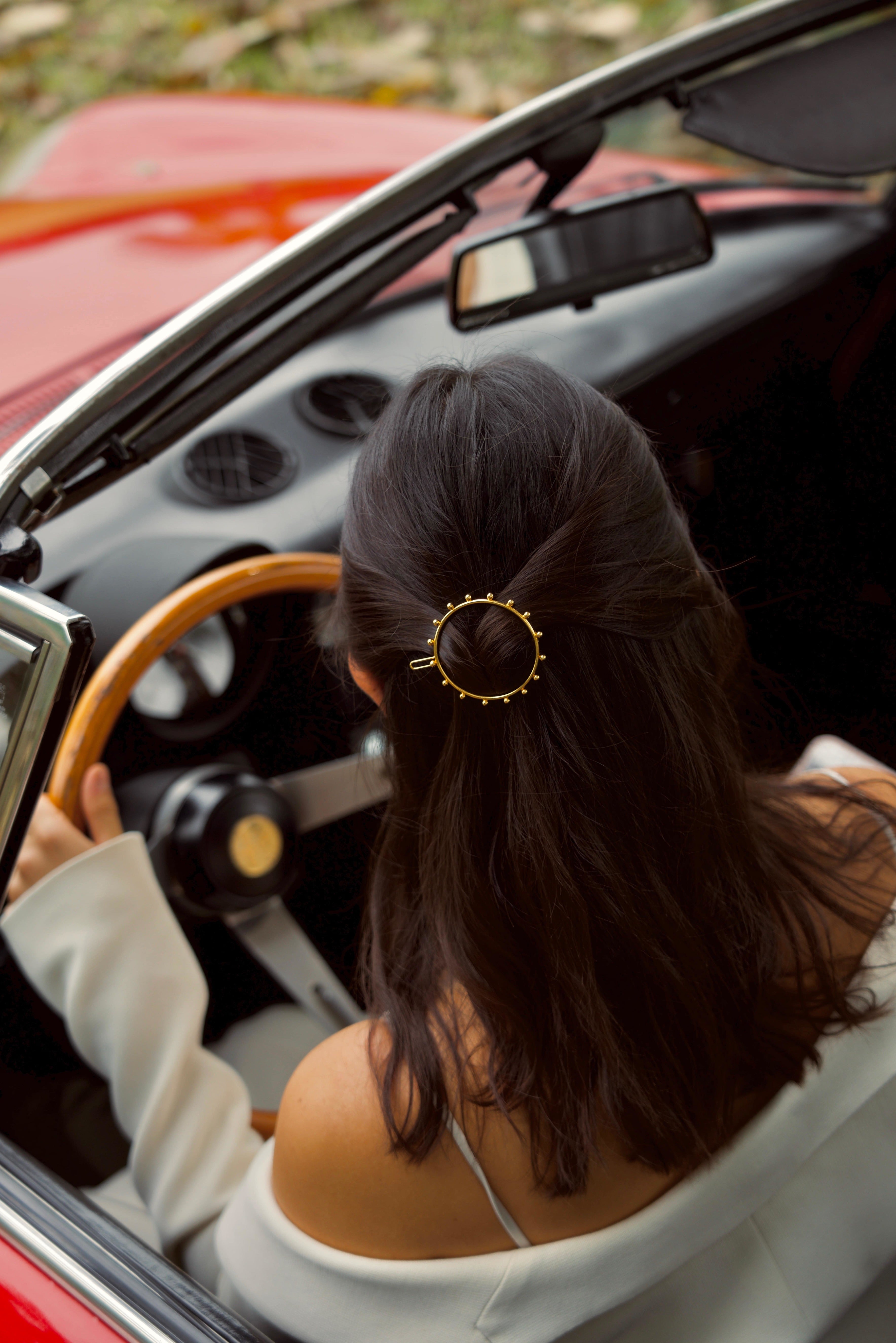 femme dans une voiture rouge portant une barrette dorée sur cheveux