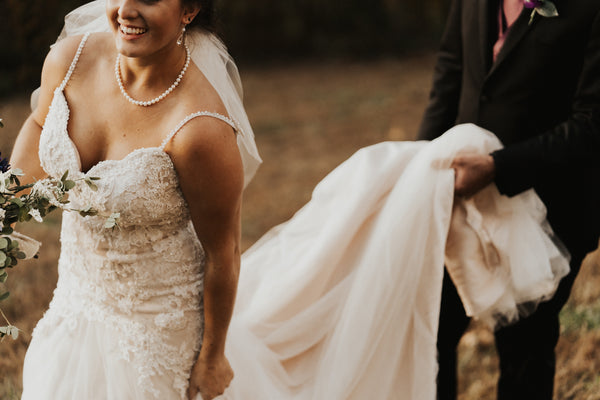 mariée en robe blanche souriante avec son mari qui lui tient sa robe