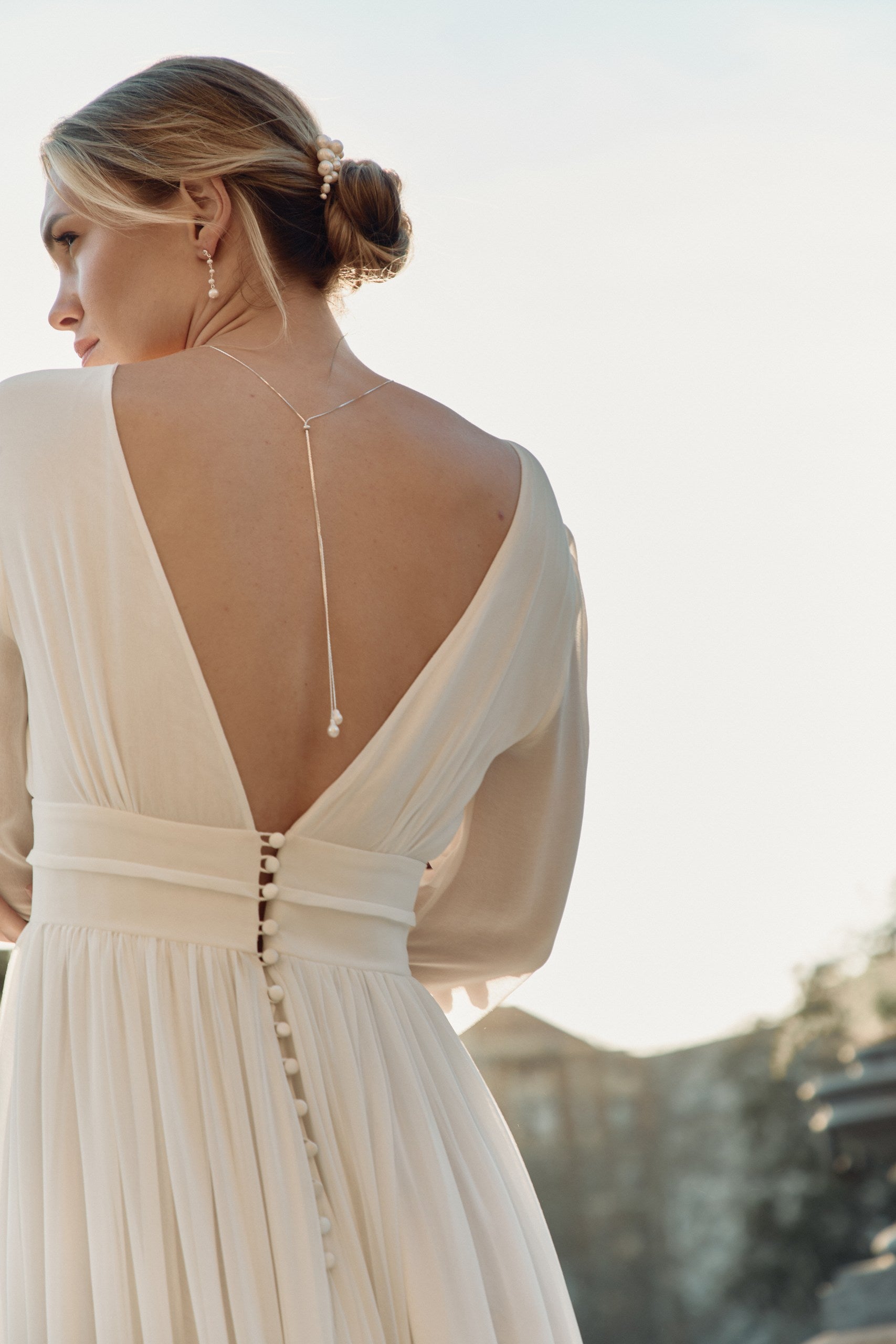 Femme de dos arborant un collier de dos minimaliste avec des pierres baroques et portant une robe de mariées avec un grand décolleté de dos