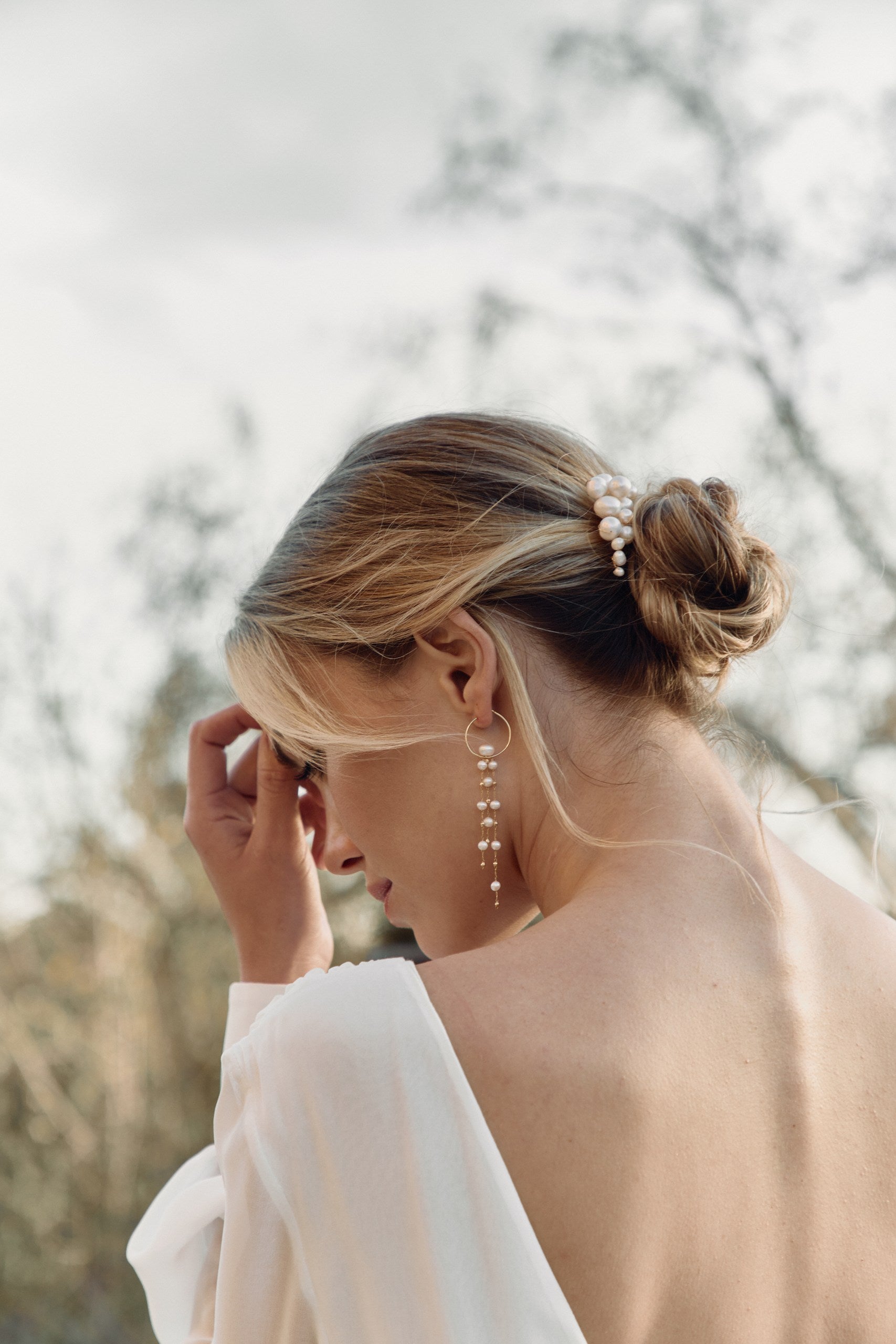 Mariée arborant des boucles d'oreilles uniques avec un anneau et des perles naturelles ainsi qu'un peigne de cheveux en forme de nuage avec des perles naturelles de différente tailles
