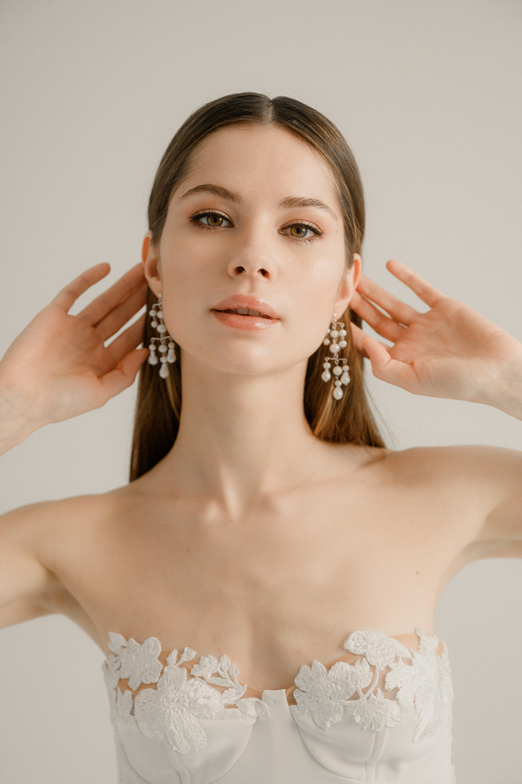 jeune femme de face regardant droit devant elle avec les mains derrière les oreilles pour montrer ses boucles d'oreilles en perles naturelles