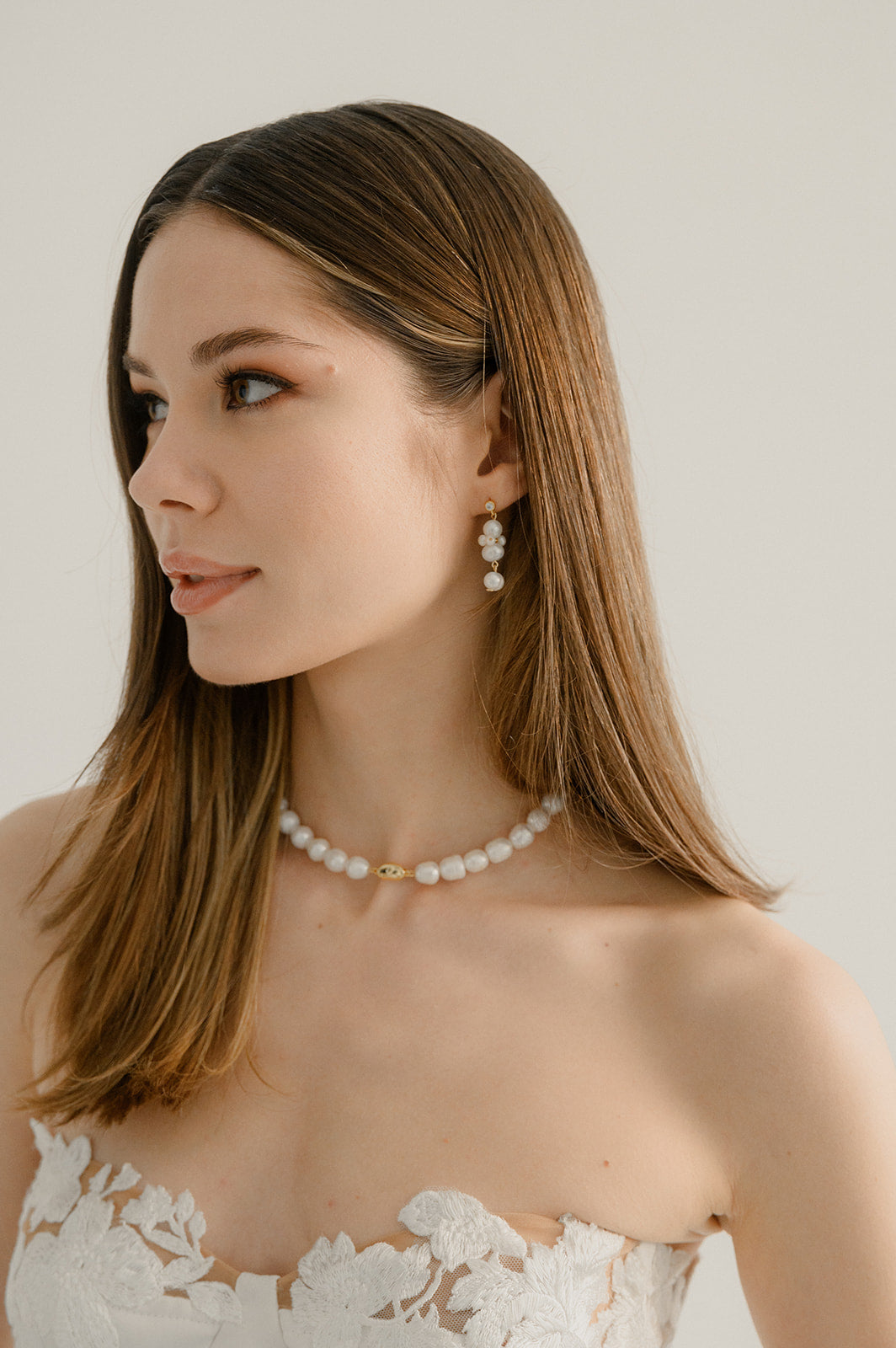 Femme qui regarde sur le côté avec les cheveux lachés montrant ses bijoux de mariage notamment son collier de perles naturelles épaisses et ces boucles d'oreilles abstraites