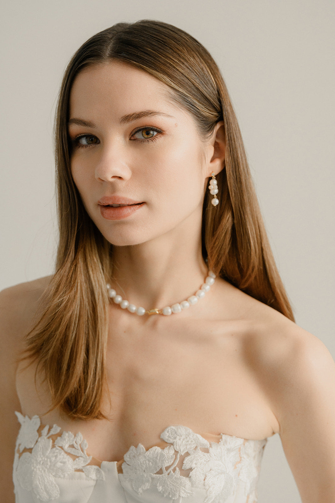 femme qui regarde devant elle portant une robe de mariée en dentelle et un collier de perles naturelles