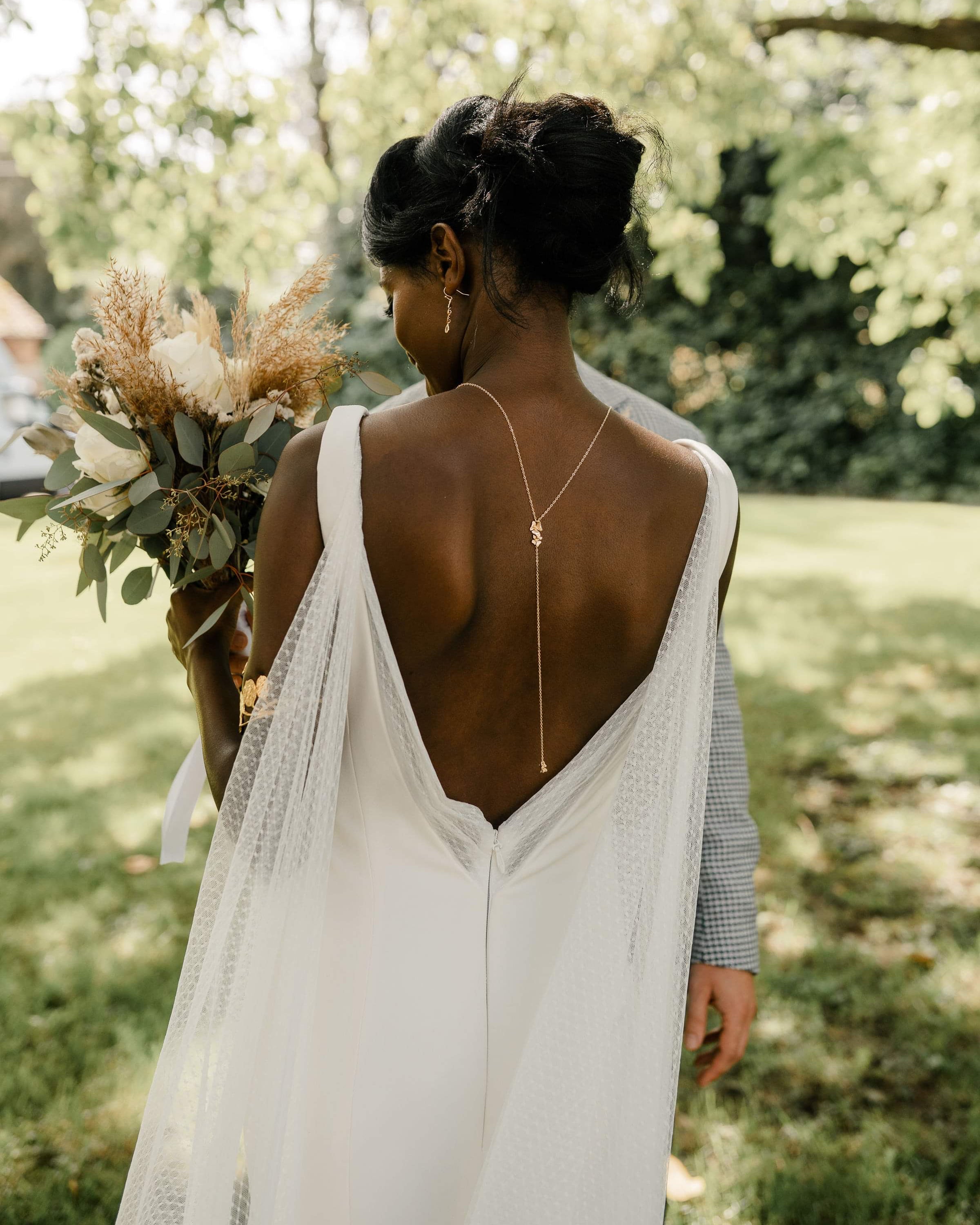 mariée le jour de son mariage portant un robe blanche avec du tulle et un décolleté de dos plongeant et un collier de dos floral