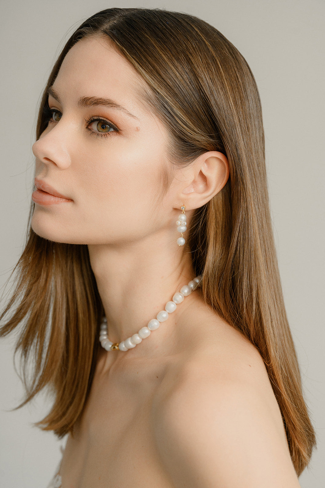 jeune femme châtain portant des boucles d'oreilles pendantes en perles naturelles et un collier assorti