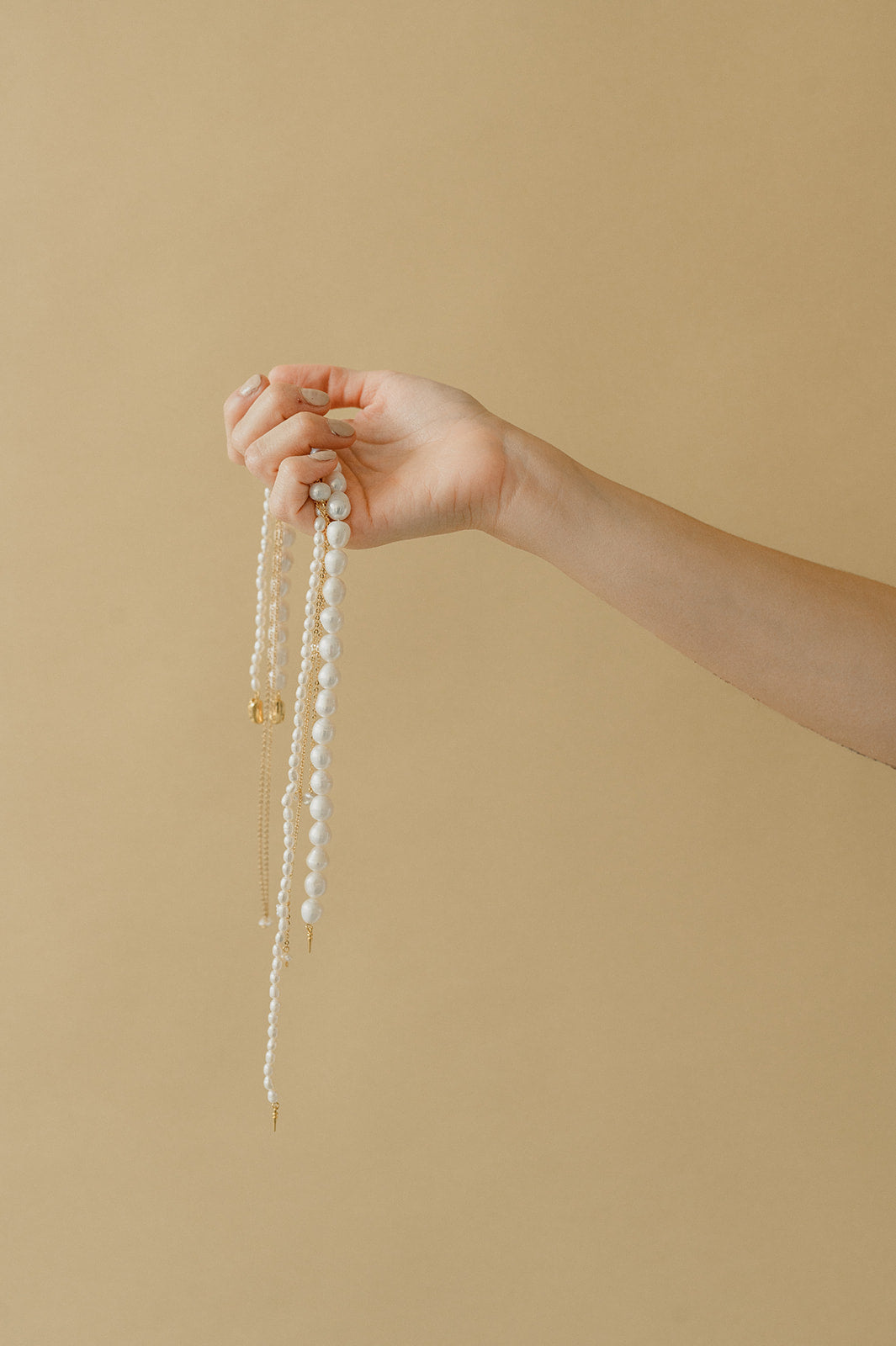 main d'une femme portant des bijoux en perles naturelles pour mariage sur un fond beige