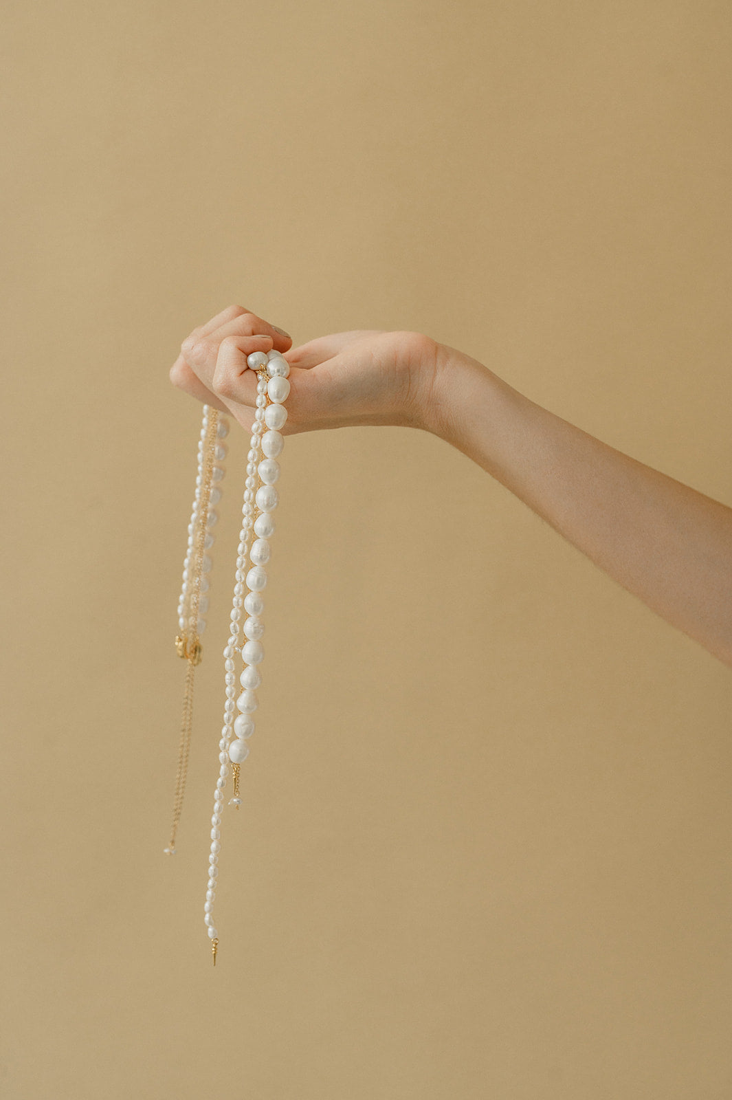 Photo d'une femme tenant des colliers de perles naturelles de mariage dans les mains avec derrière un fond unis