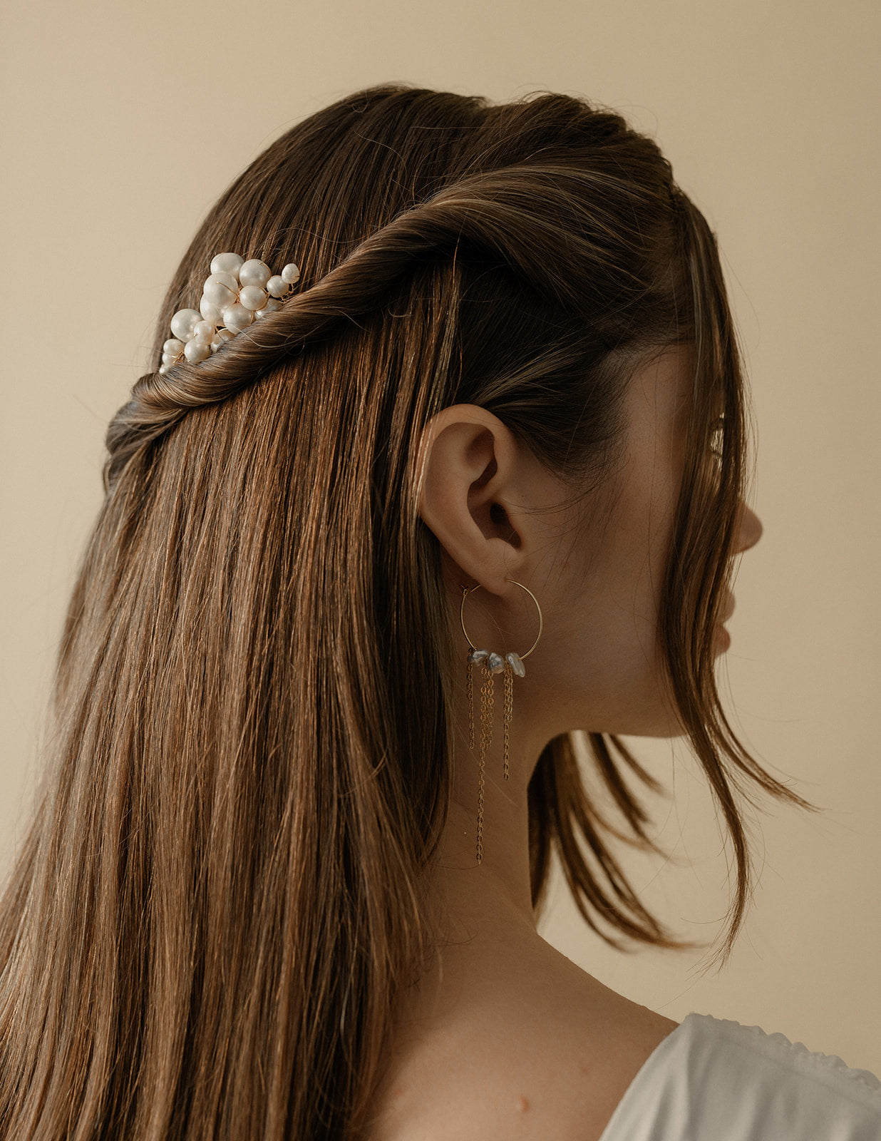 Femme sur le côté avec les cheveux long lachés montrant en avant ses boucles d'oreilles ronde et pendantes avec des perles irrégulières