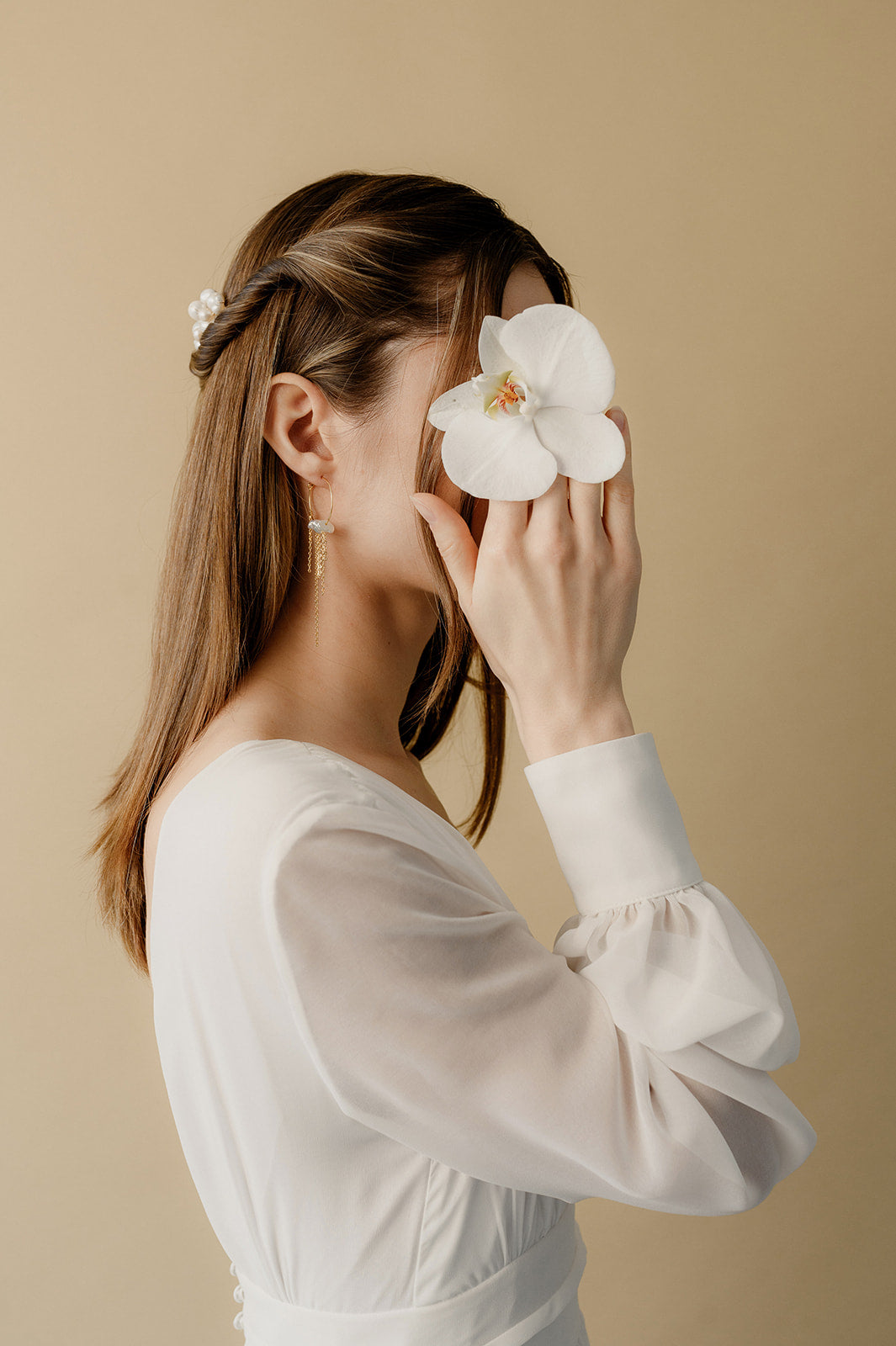 Jeune femme en robe de mariée tenant de manière esthétique une orchidée blanche dans la main cachant son visage 