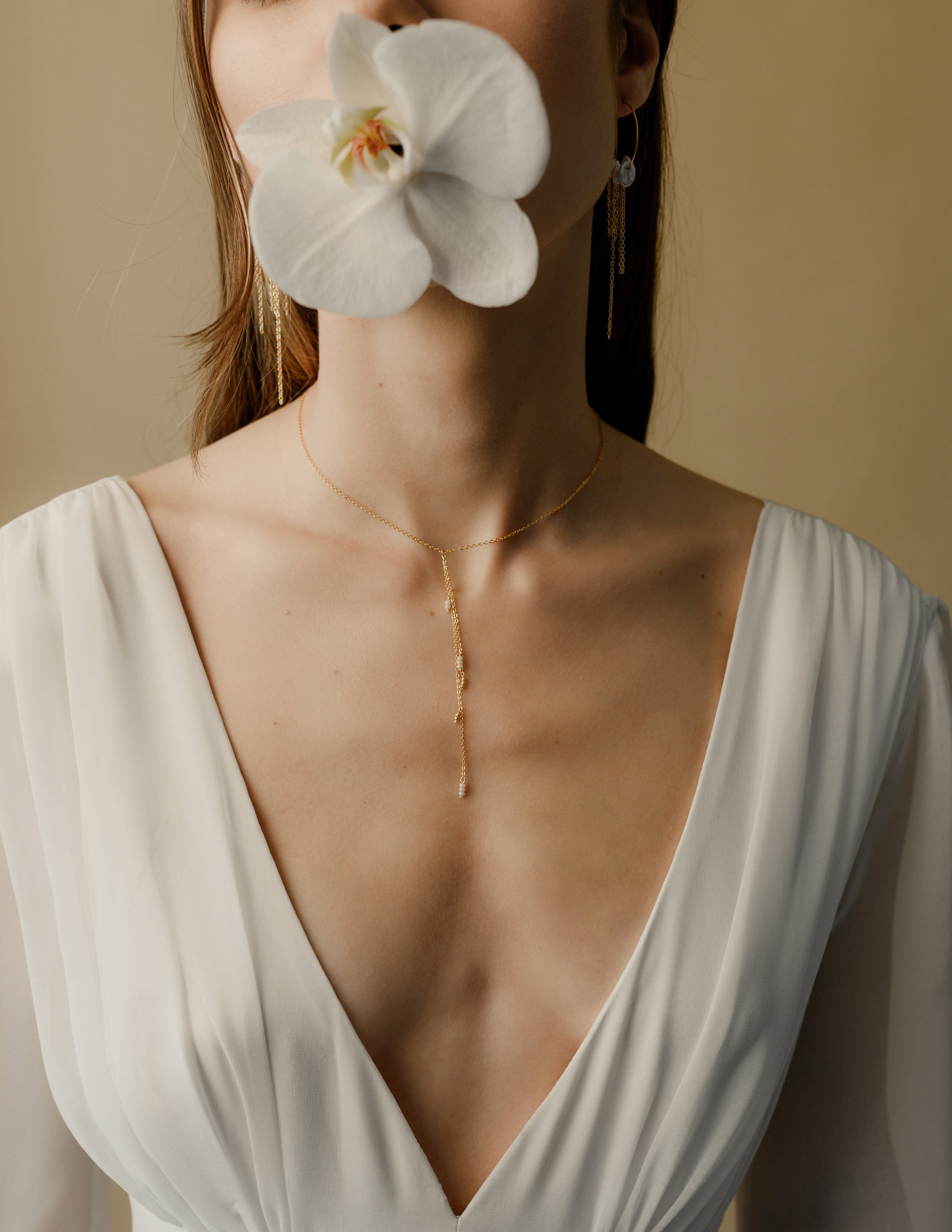 femme portant un collier pour un décolleté en V avec des perles rocailles et tenant une orchidée dans la bouge 