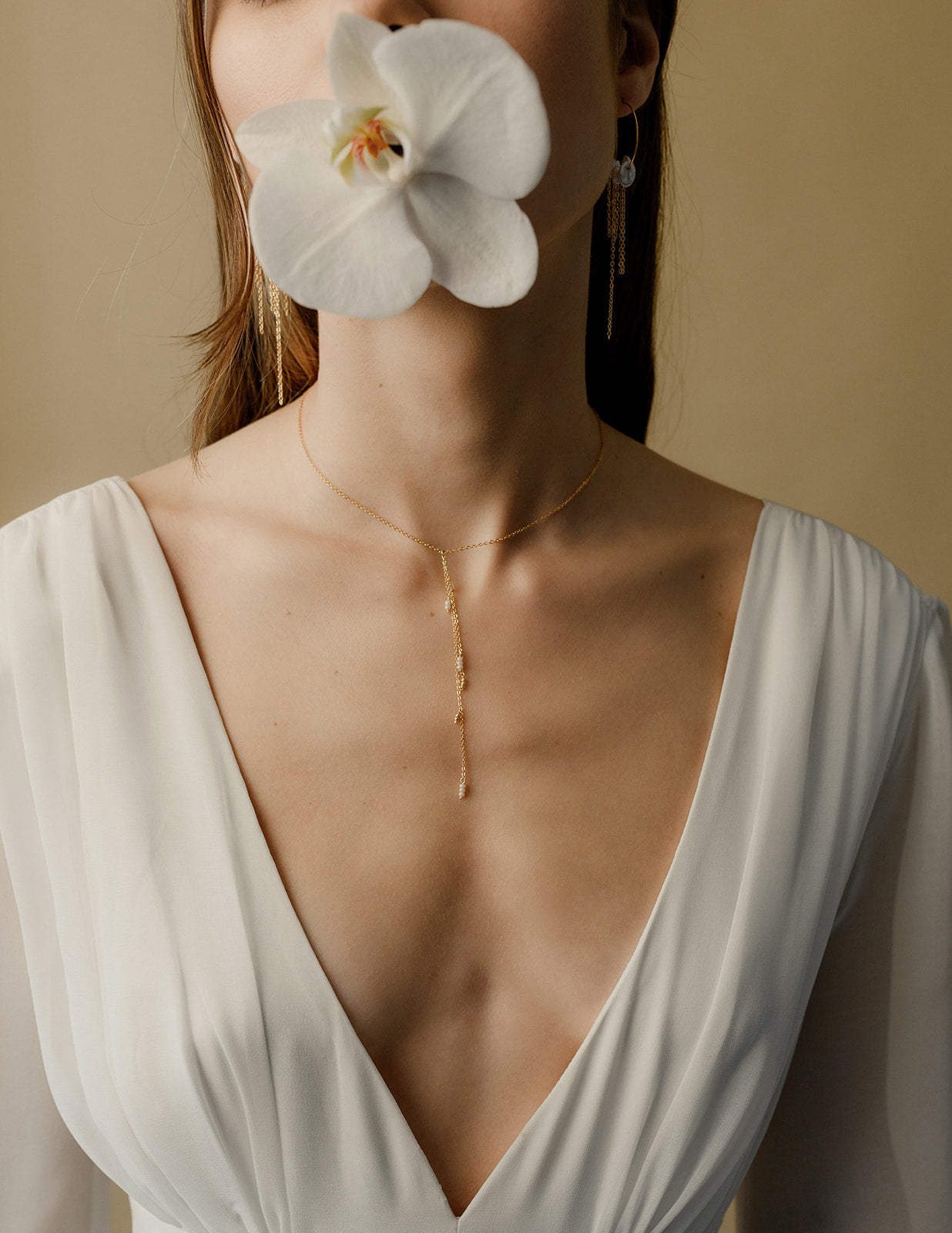 Jeune femme portant une orchidée avec une robe de mariée bohème à grand décolleté montrant son collier pendant 