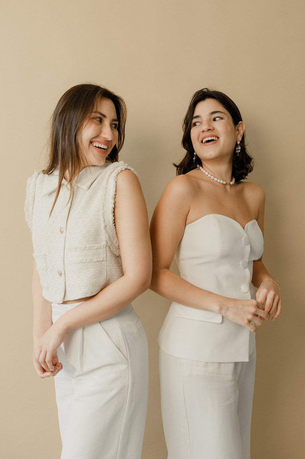 deux femmes se regardant dos à dos habillée en blanc pour un mariage sur un fond beige