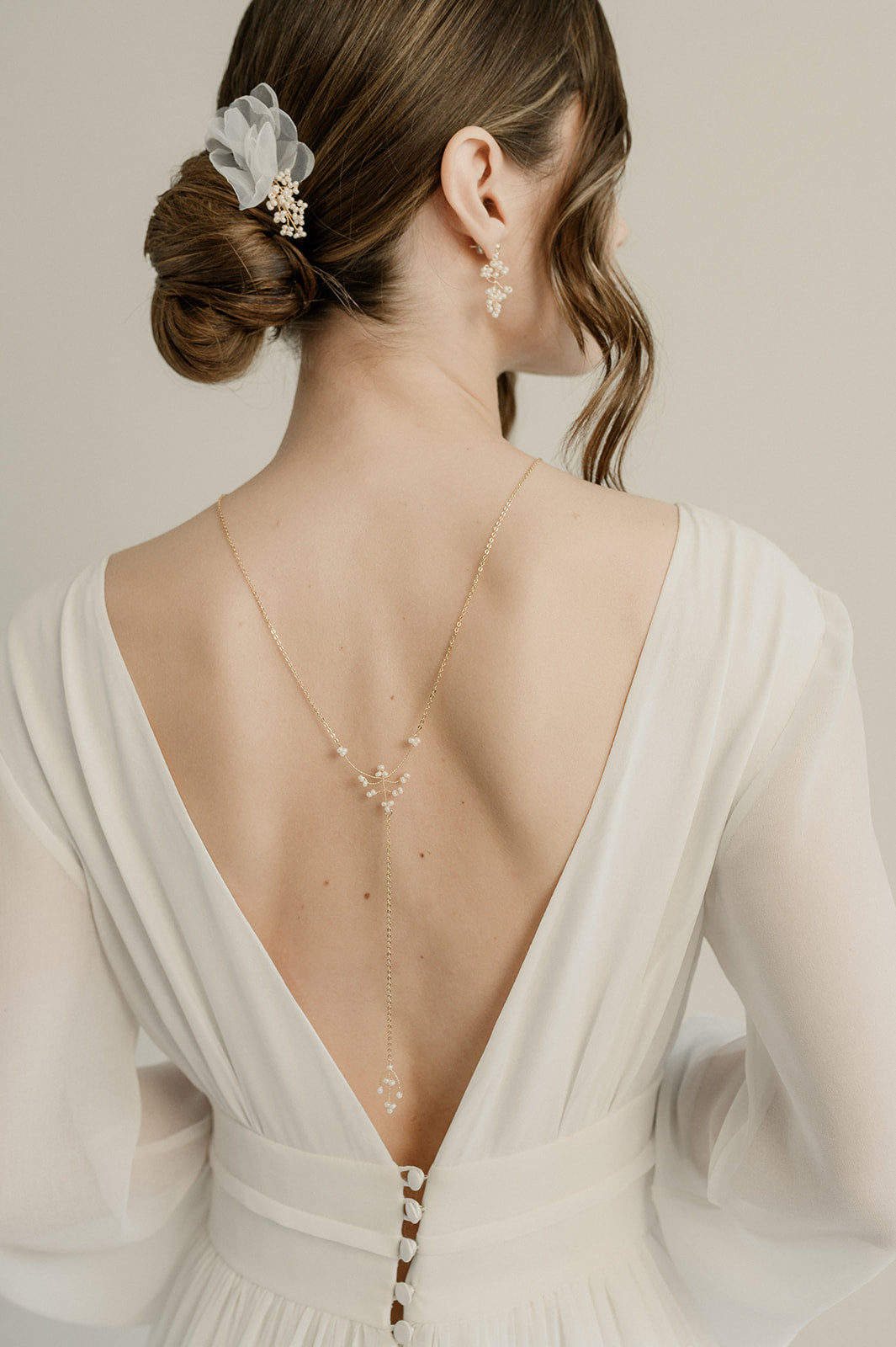 femme de dos habillée avec une robe de mariée blanche avec des boutons dans le dos portant un collier de dos avec des perles rocailles