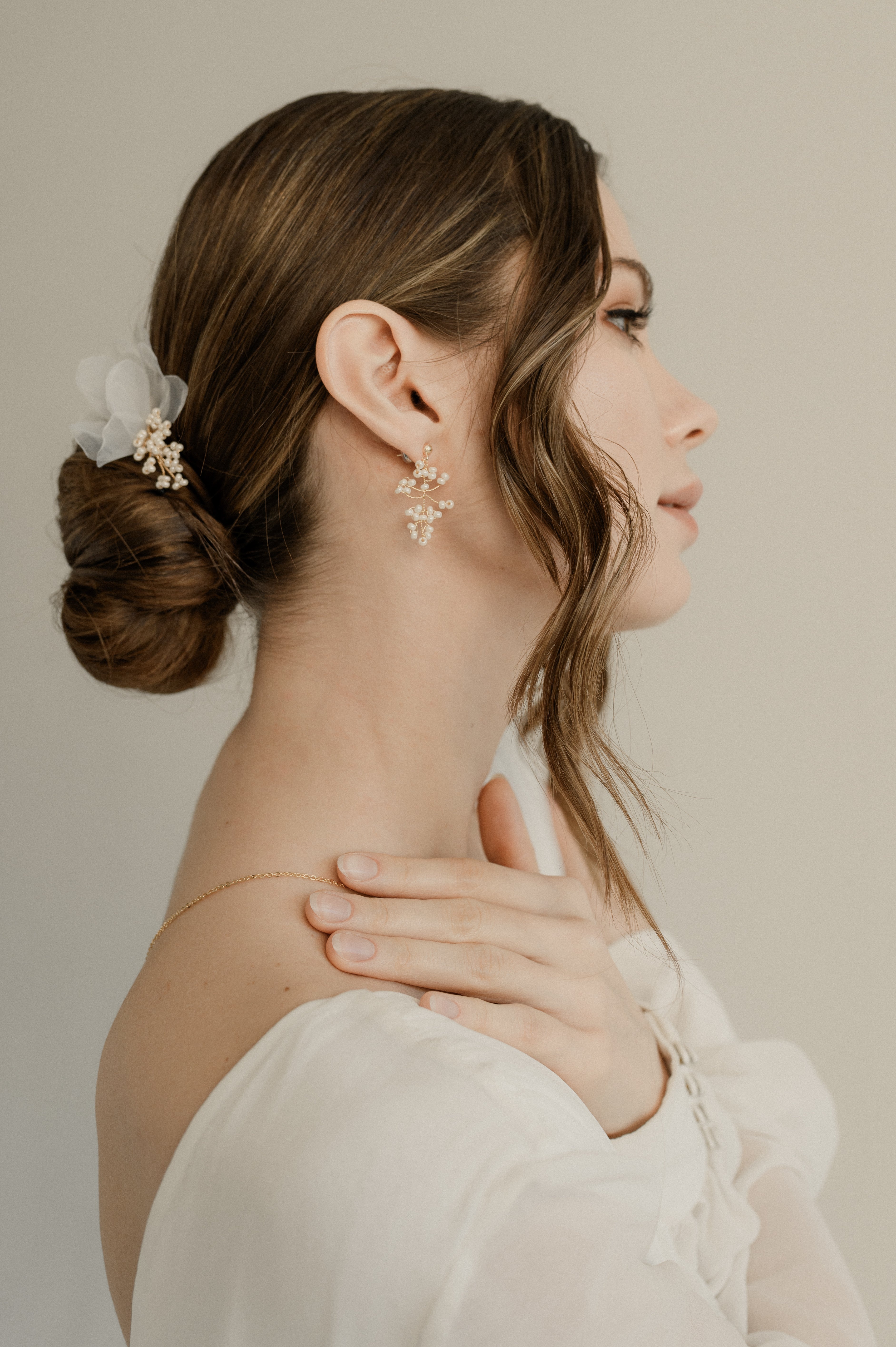 femme de profil la main sur l'épaule portant une paire de boucles d'oreilles en perles rocailles et un accessoire de cheveux sur son chignon