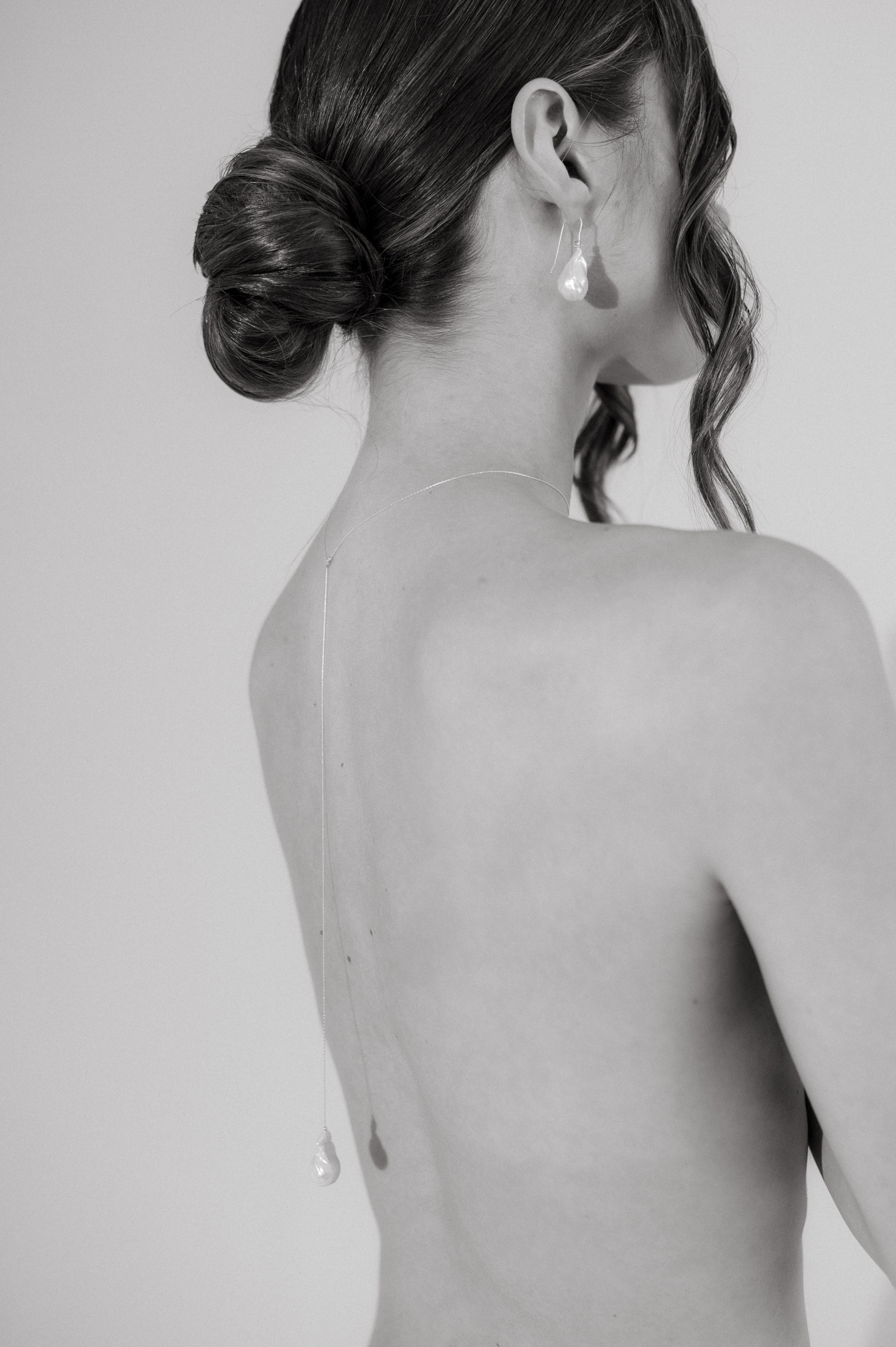 femme de dos en noir et blanc qui porte un collier de dos avec un pendentif perle baroque