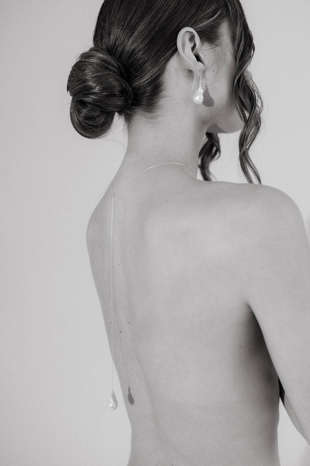 femme en noir et blanc de dos qui porte un collier de dos en perle naturelle baroque et un chignon 