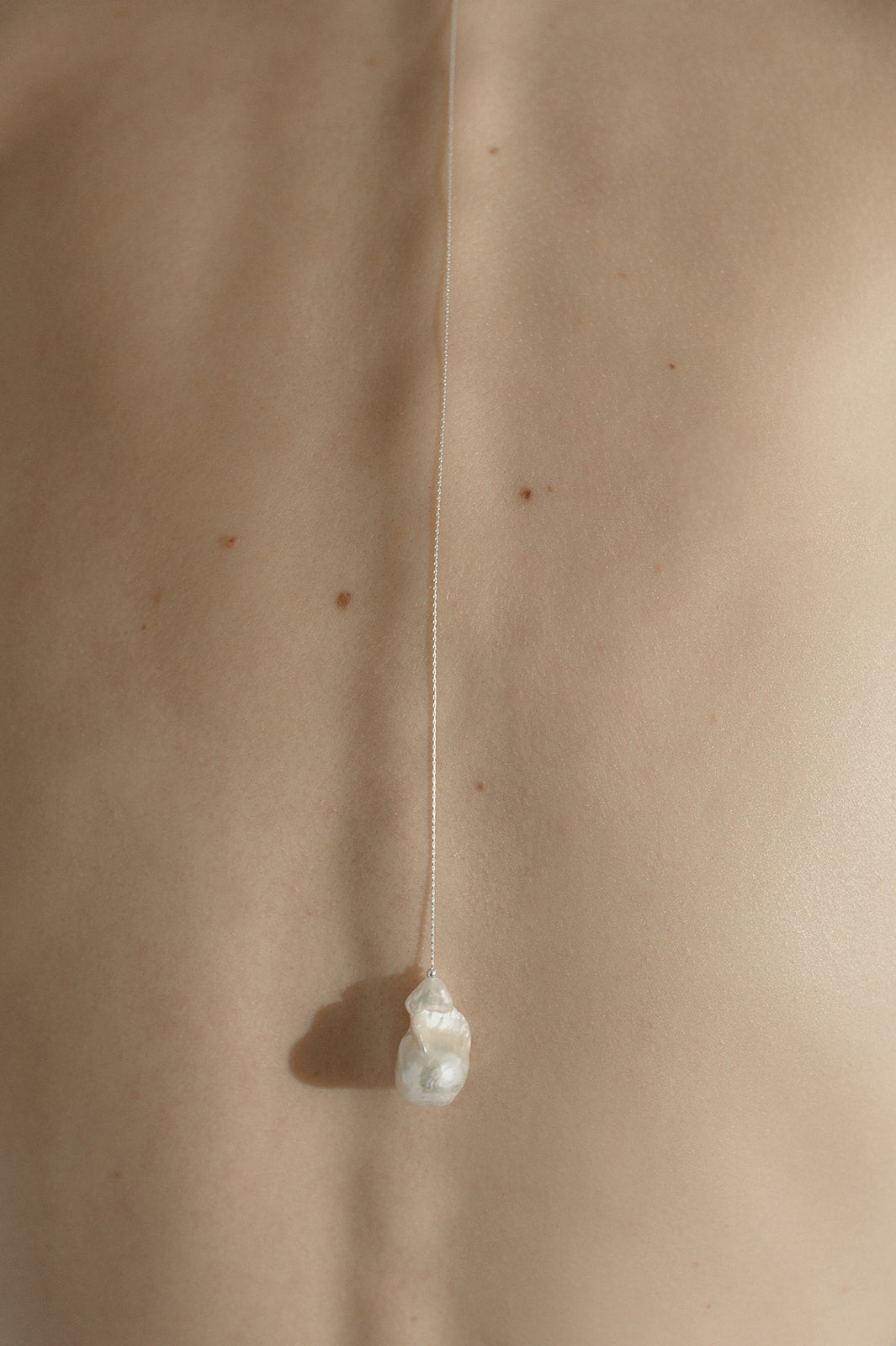 gros zoom sur le dos d'une femme portant un collier de dos avec une perle naturelle baroque
