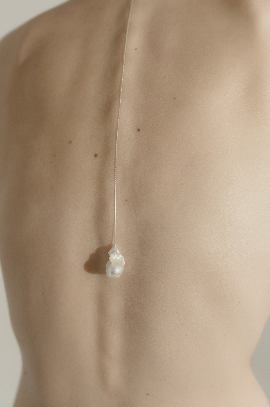 dos d'une femme portant un collier de dos argenté avec une perle naturelle baroque