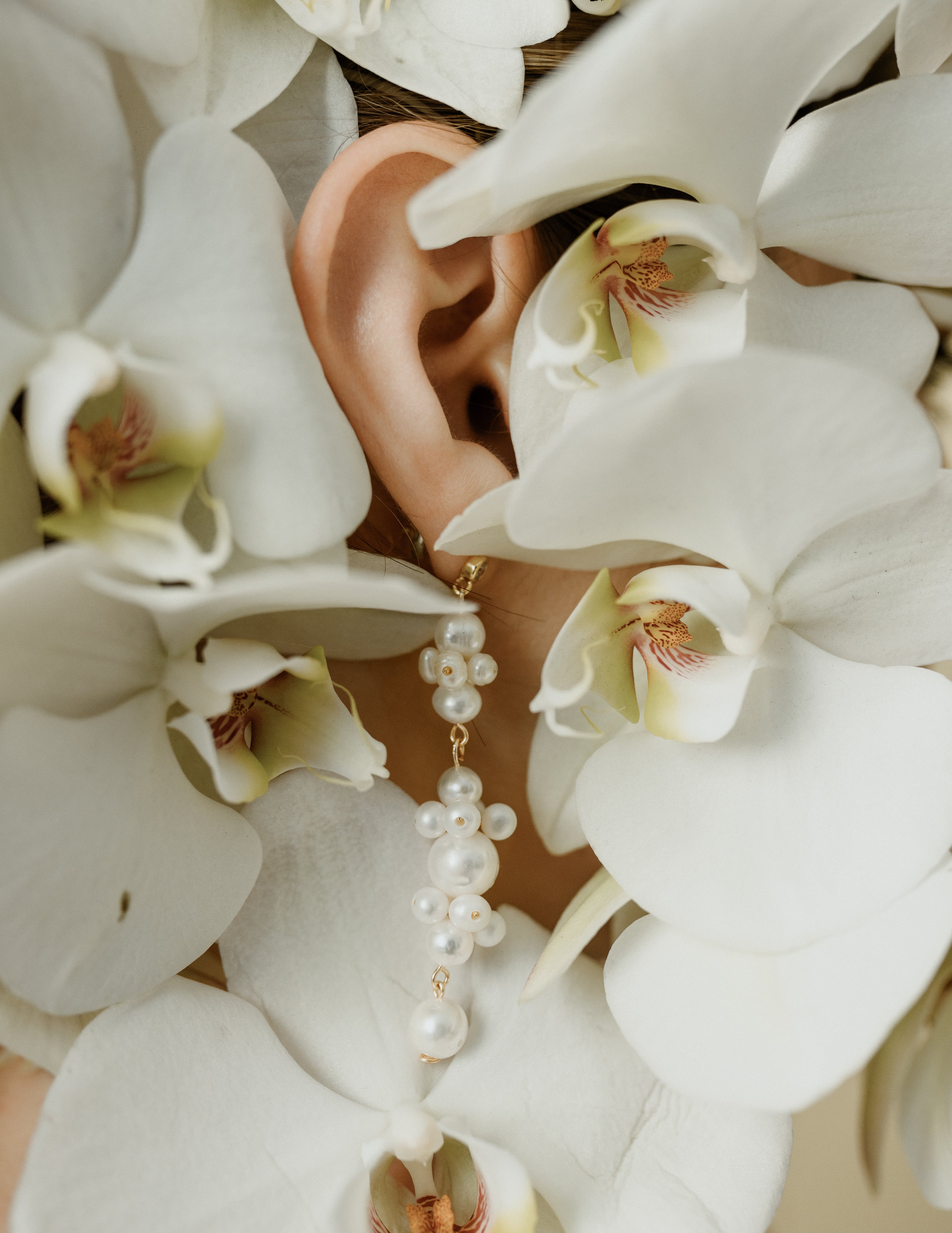 oreille d'une femme portant des boucles d'oreilles en perle naturelles et or ornée d'orchidée blanche